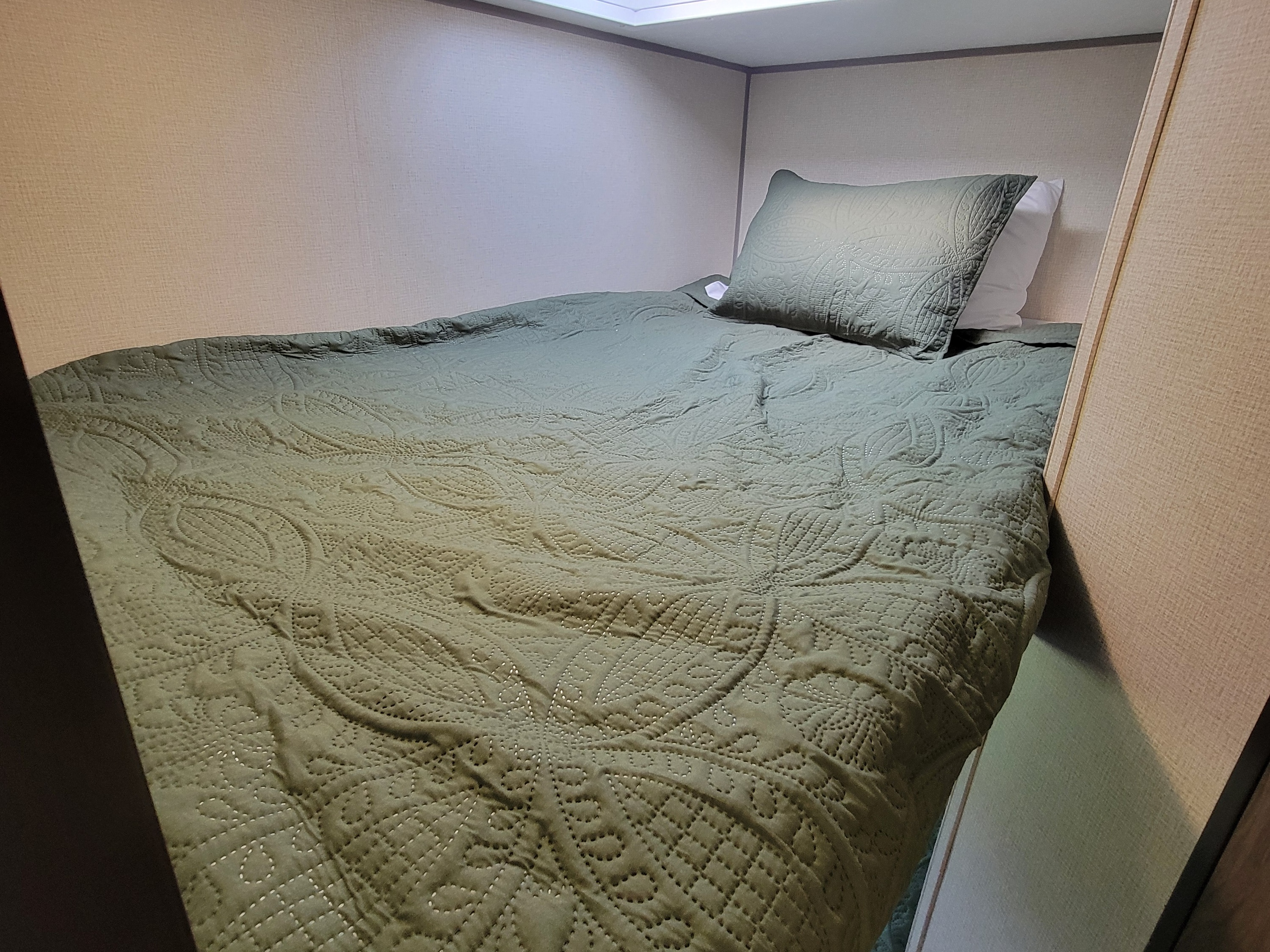 Cozy RV rental bunk bed with an olive green quilted comforter and pillow, offering a comfortable sleeping space.. Forest River Avenger 2020