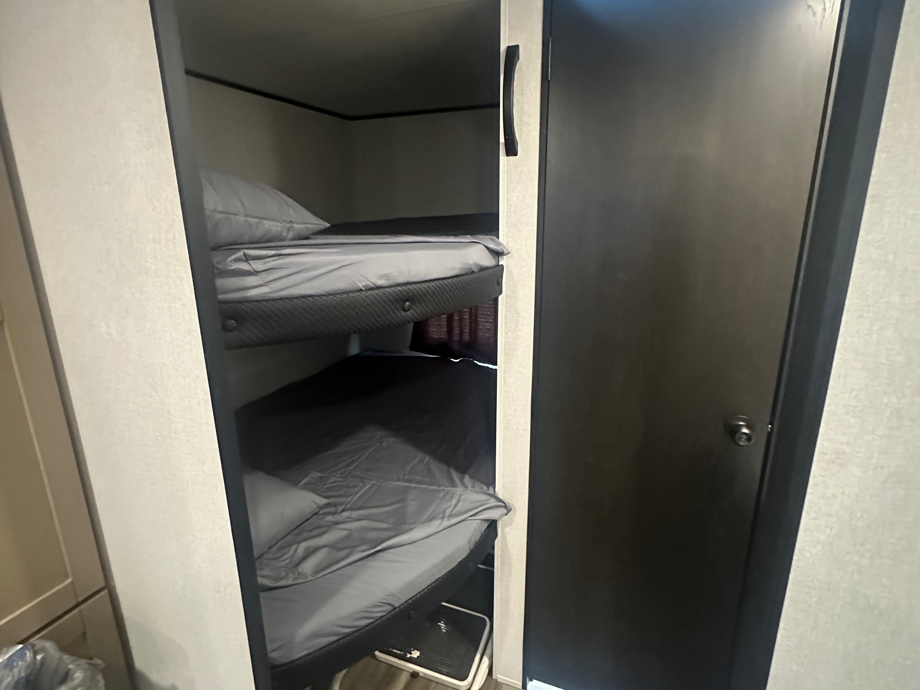 This RV rental features two neatly made bunk beds with gray sheets and pillows, offering comfortable sleeping next to a dark door.. Colt Open range 26dbs 2026