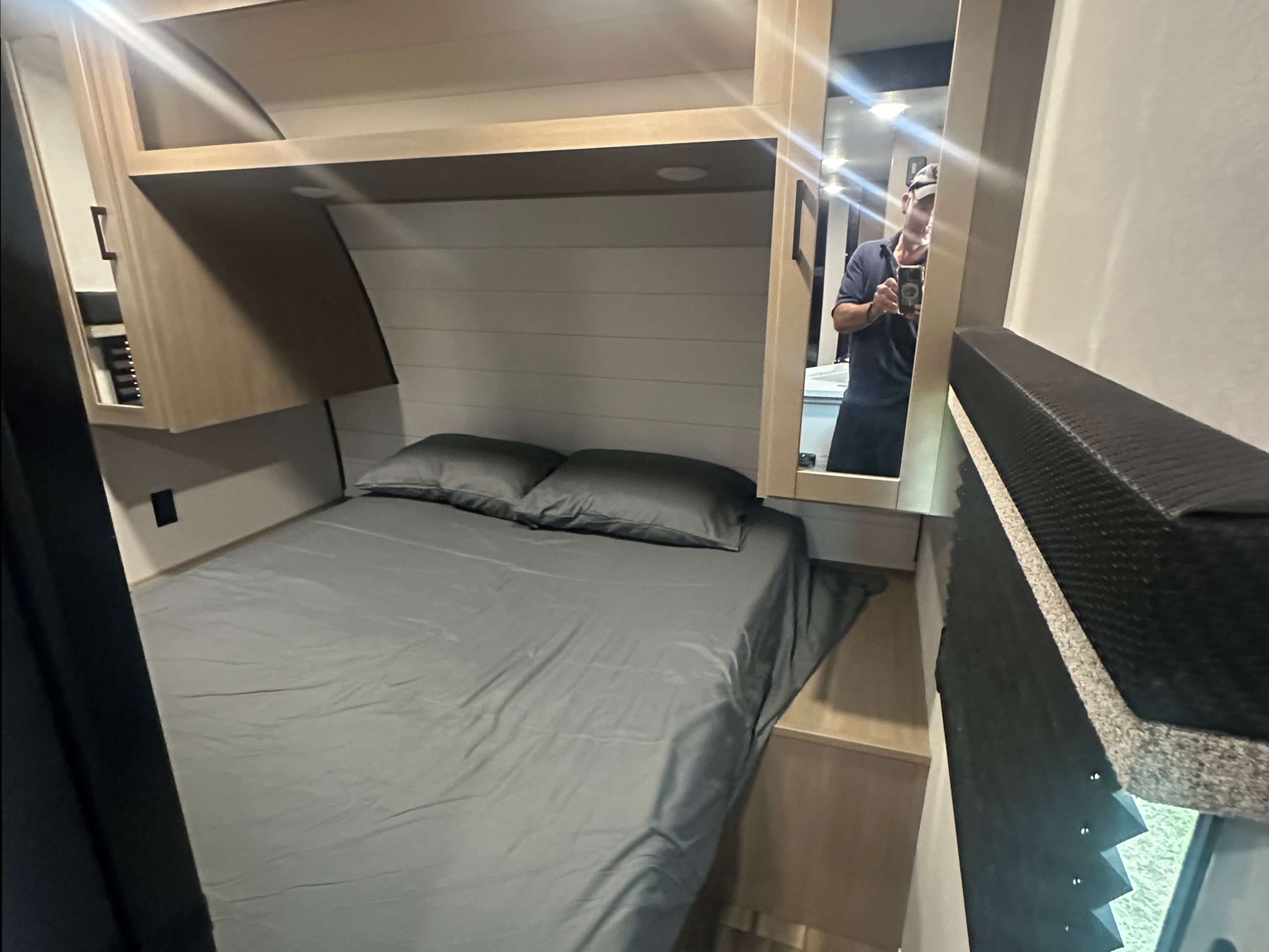 Cozy RV rental bedroom with a grey bed, overhead cabinets, and a mirror, offering comfortable sleeping for travelers.. Colt Open range 26dbs 2026