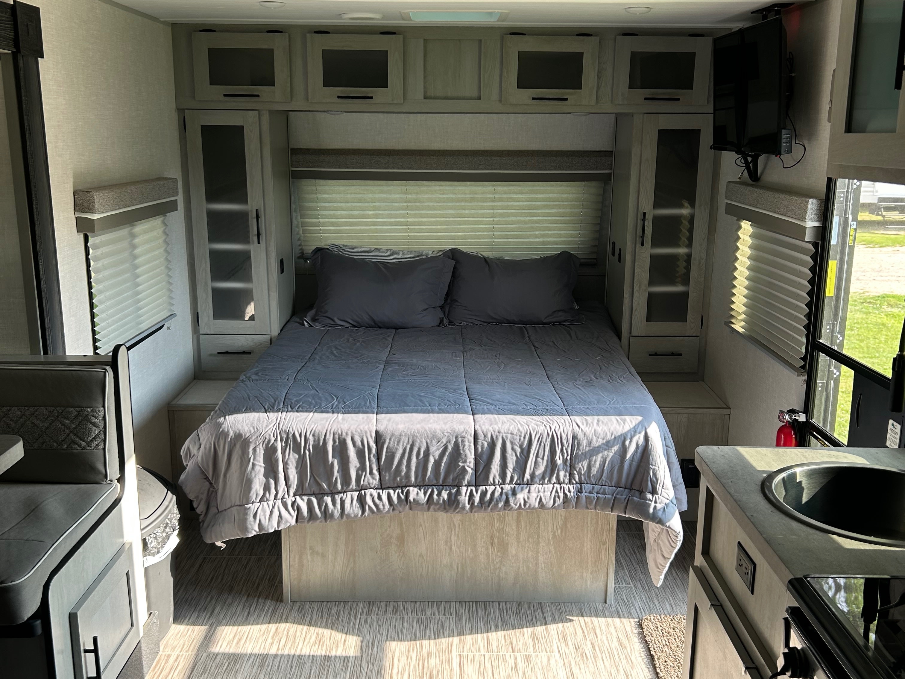 Inside a modern rv rental: grey bed, overhead cabinets, wall-mounted TV, and compact kitchen/dinette area.. Forest River Ibex 2022