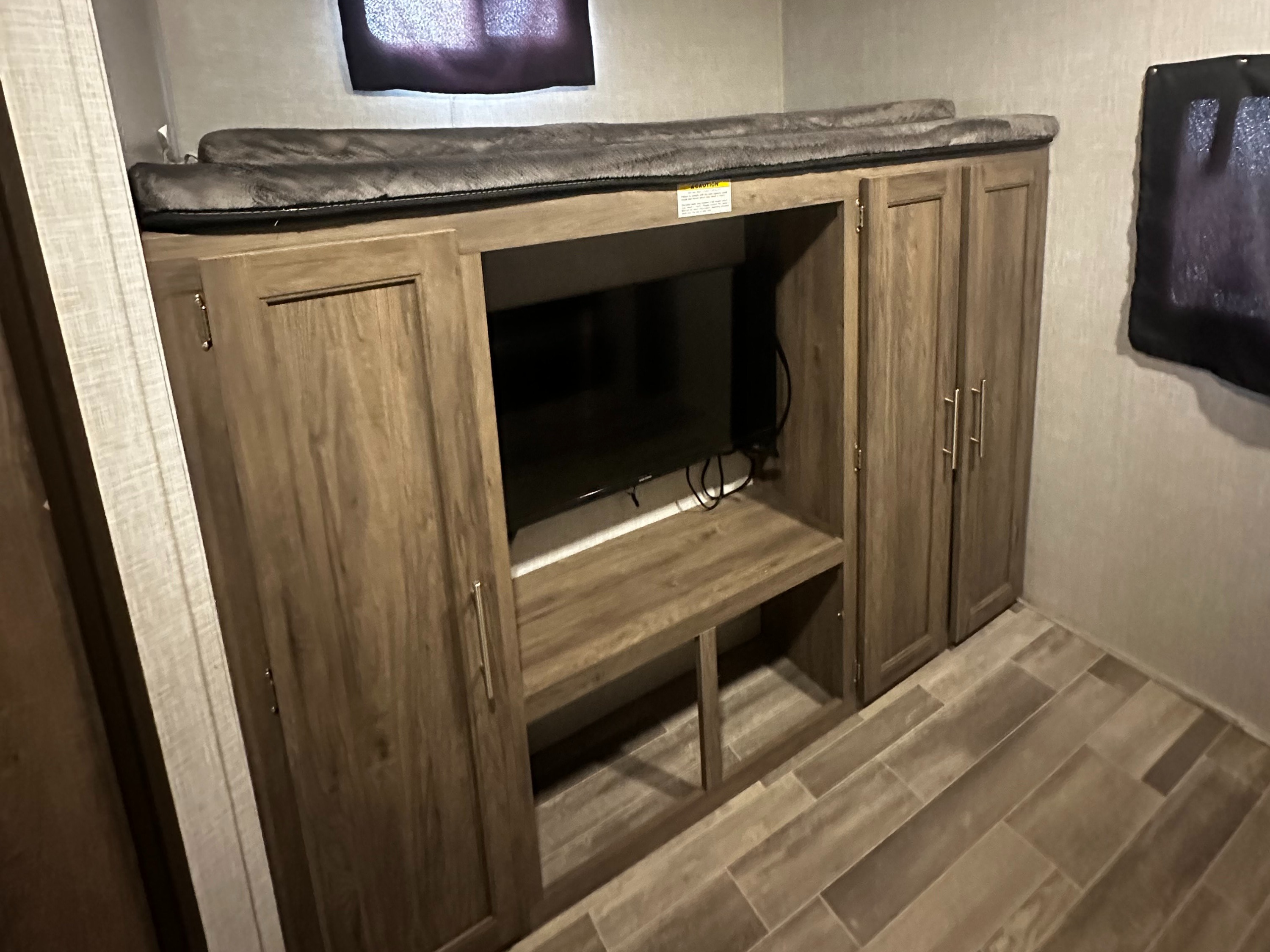 RV rental interior: bunk beds over a TV entertainment unit with storage, featuring a ceiling AC unit and wood-look plank flooring.. Crossroads RV Zinger 2020