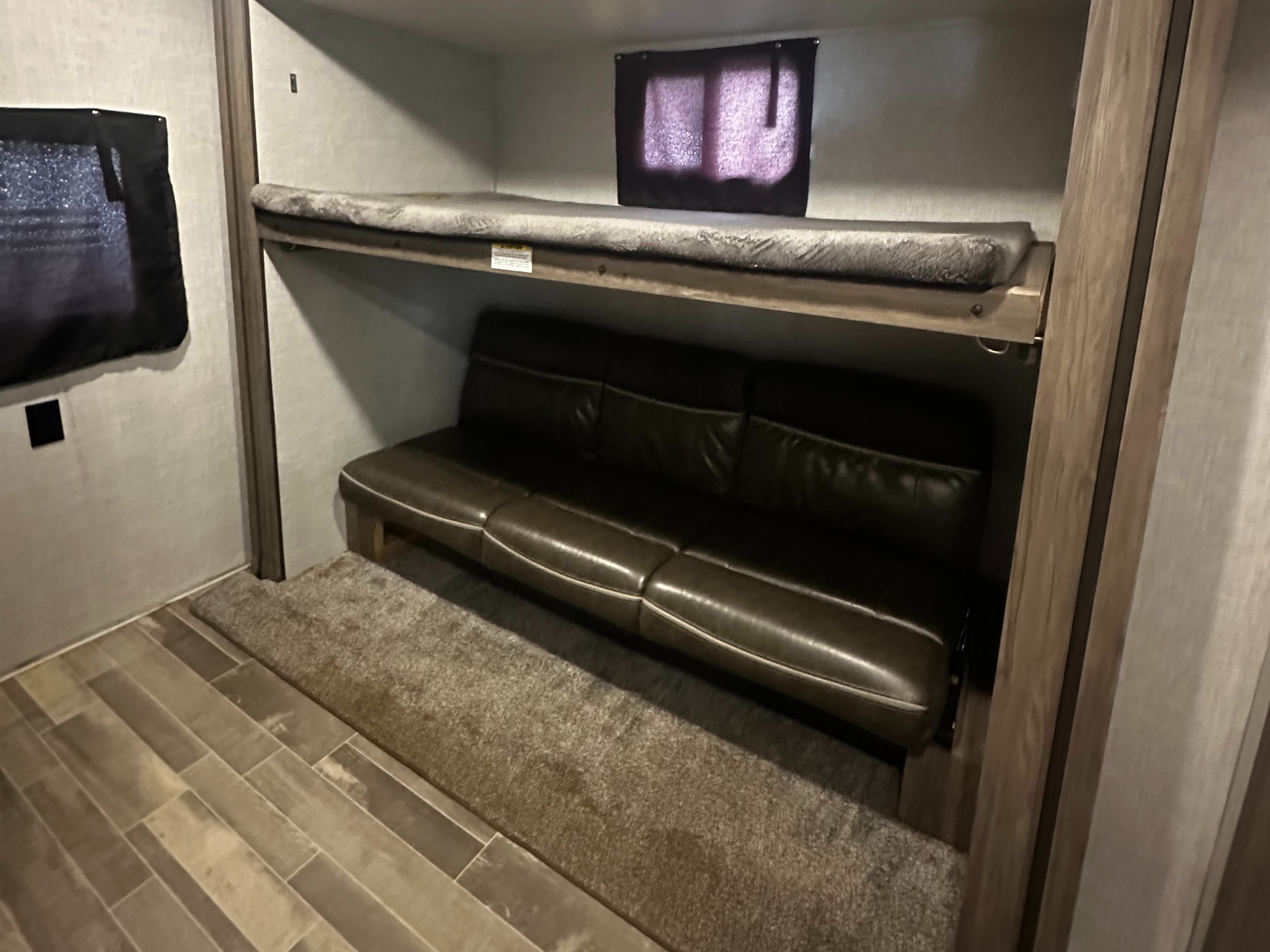 RV rental interior featuring bunk beds: an upper bed with a grey mattress and a lower brown sofa, on wood-look flooring.. Crossroads RV Zinger 2020