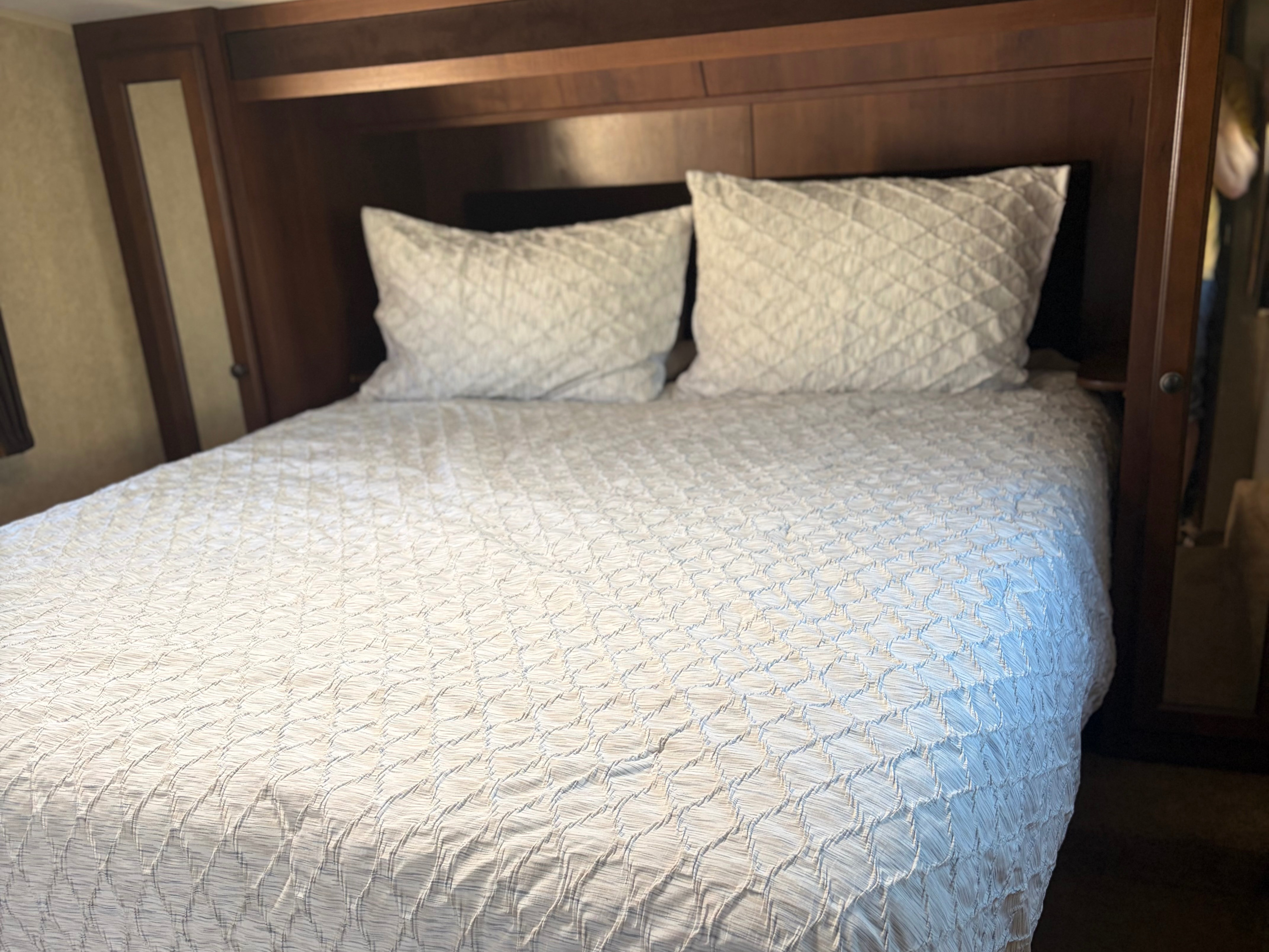 Clean RV rental bedroom: cozy white quilted bed, pillows, and wood paneling for a comfortable stay.. Jayco Eagle HT 2014