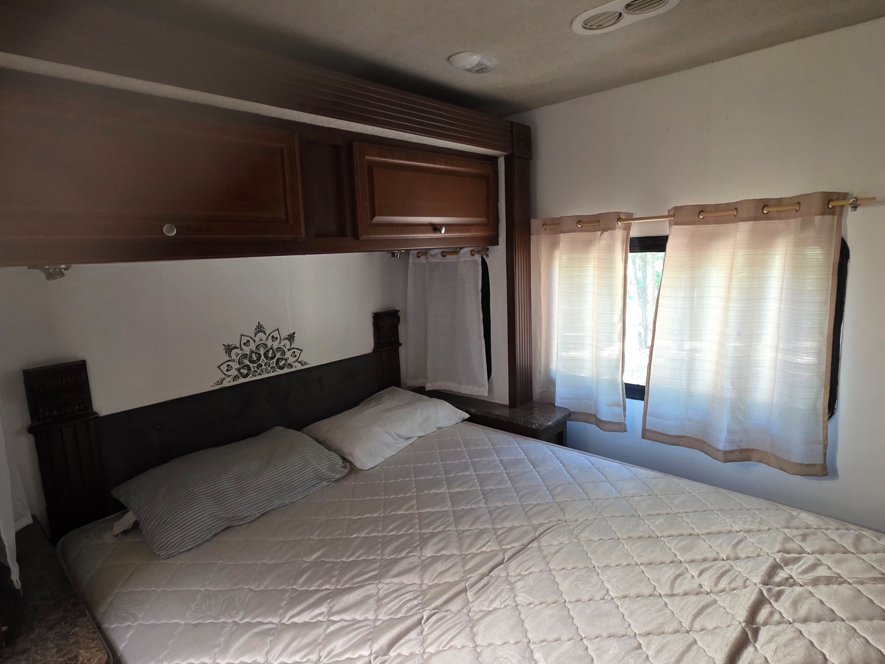 RV rental bedroom: a bed with pillows, wood cabinets, decorative wall decal, and windows with sheer curtains.. Jamboree Searcher 2014