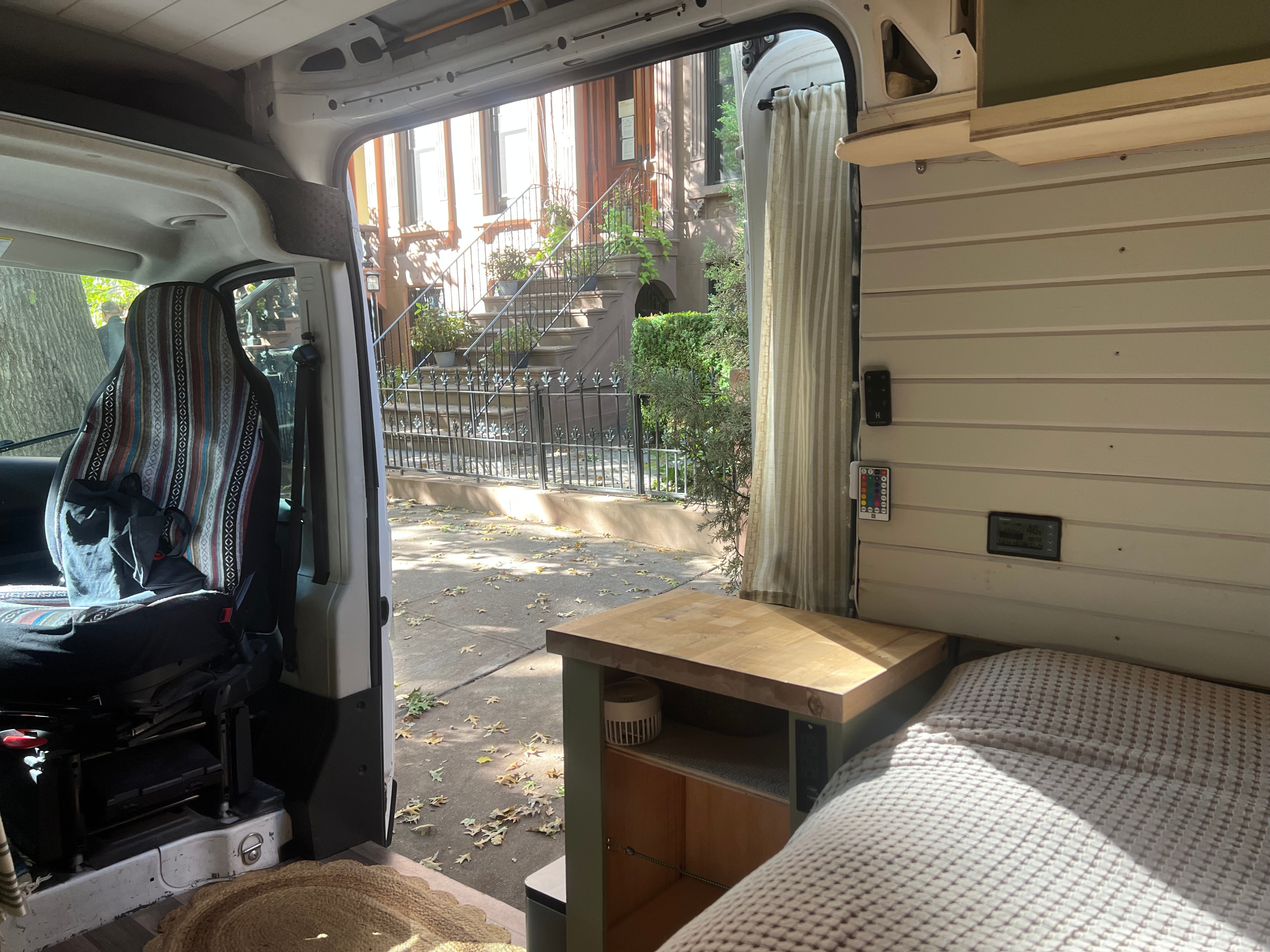 Inside a cozy RV rental camper van, with the open side door revealing a charming street of brownstones and autumn leaves.. Dodge Promaster 2500 high roof 2019