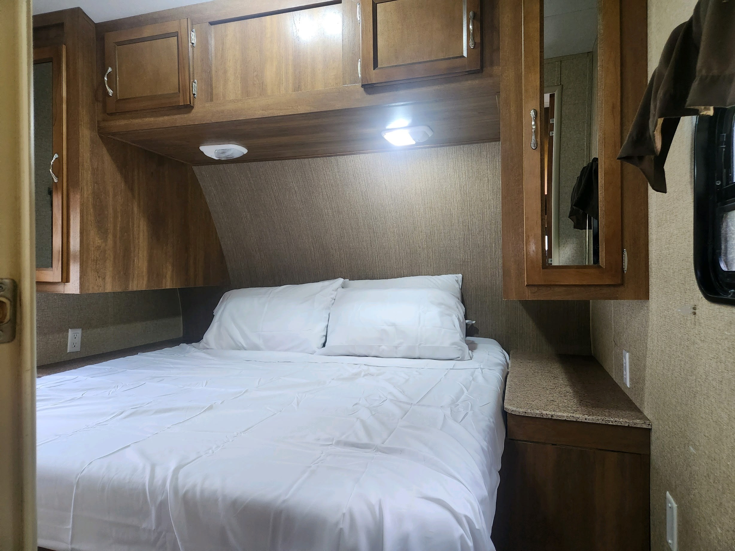 Cozy RV rental bedroom featuring a bed with white linens, overhead wooden cabinets, and integrated bedside storage.. Coachmen Catalina 293qbck 2015