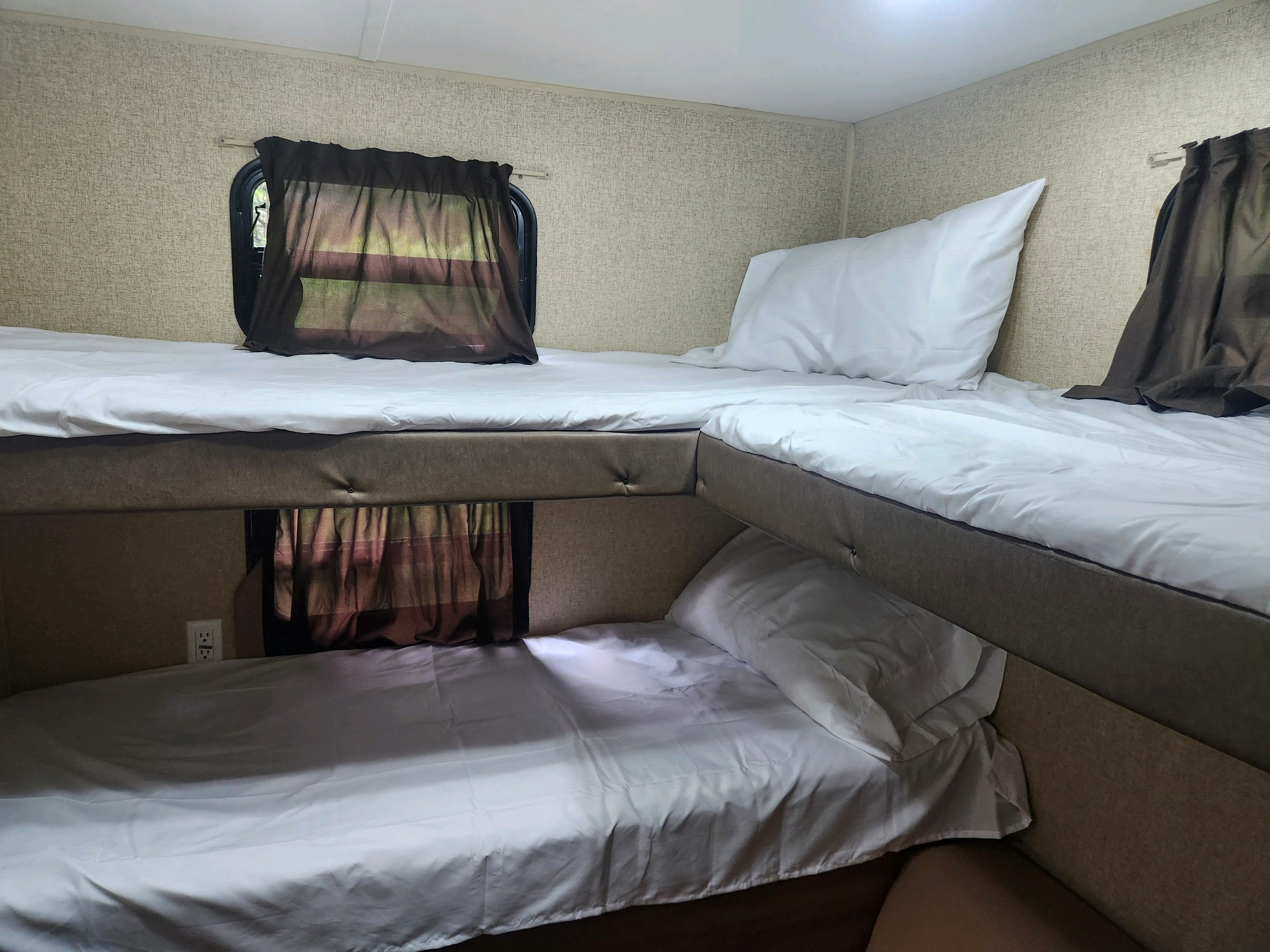 Cozy bunk beds with white bedding and brown curtains in an RV rental, offering comfortable sleeping for travelers.. Coachmen Catalina 293qbck 2015