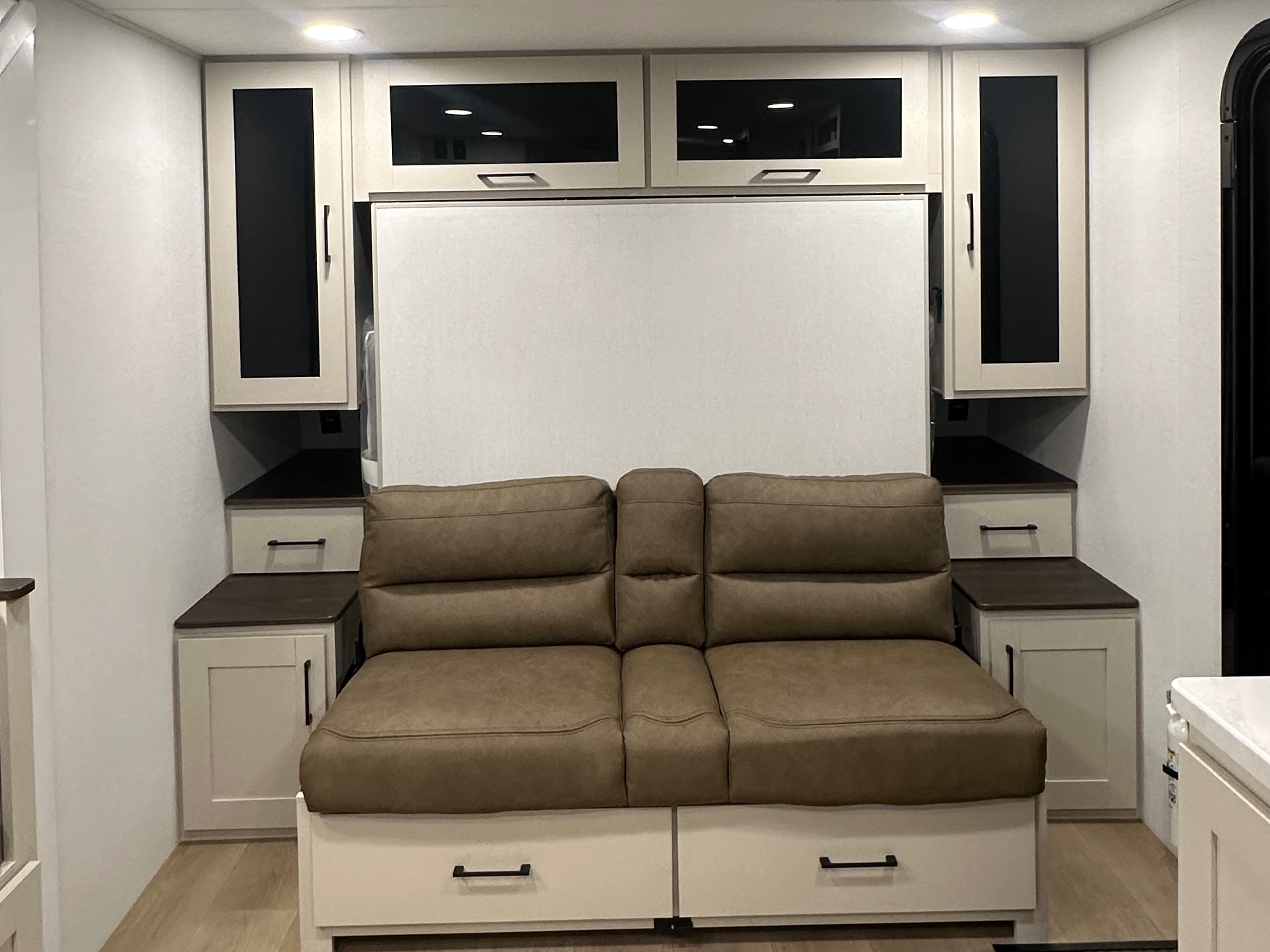 Cozy brown sofa and integrated light cabinets with dark glass in an RV rental. Built-in storage optimizes space for travel.. Alliance Delta BH181 2027