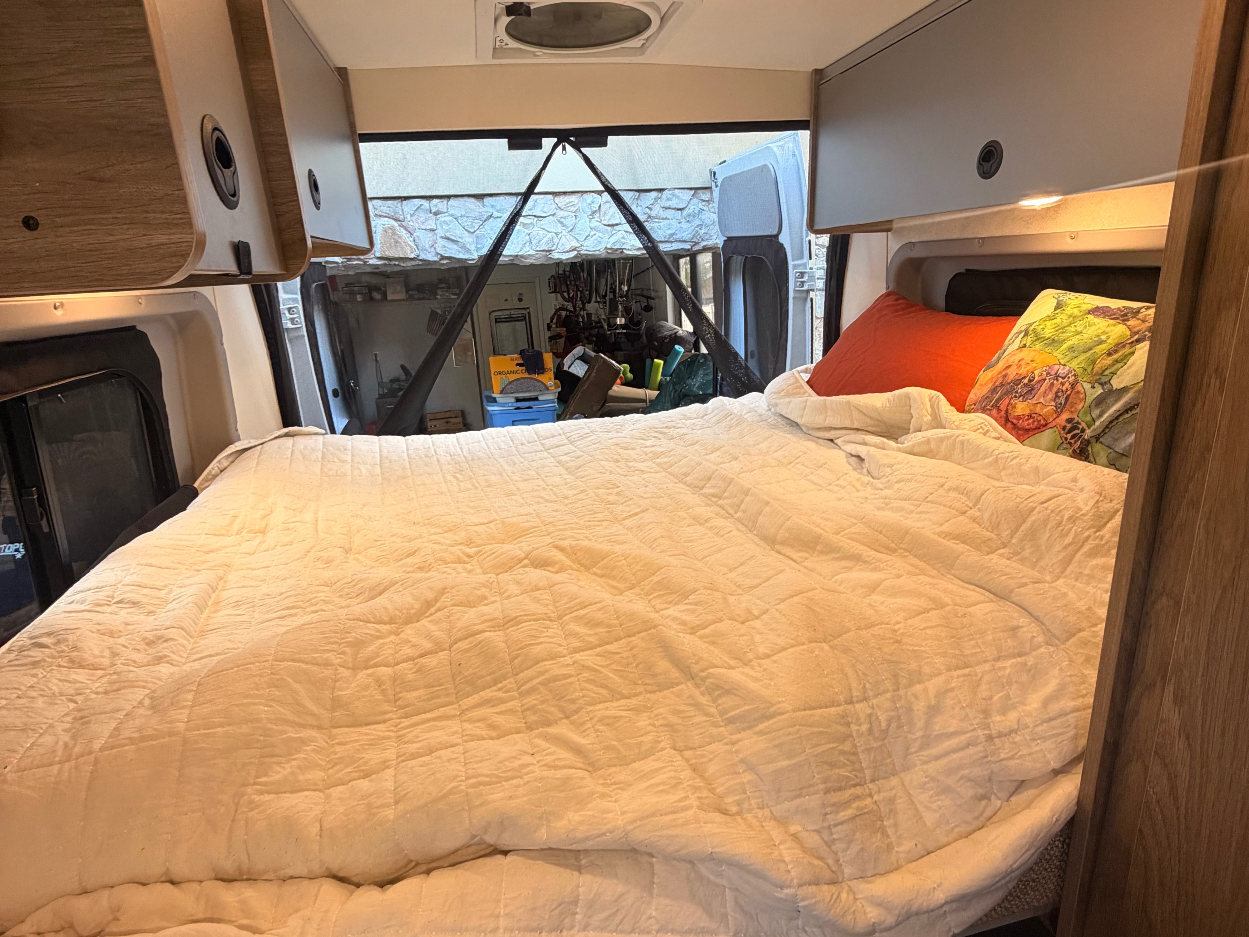 Cozy RV rental interior features a comfortable, quilted bed, overhead storage, and an open view through the back doors.. Winnebago Winnebago 2023