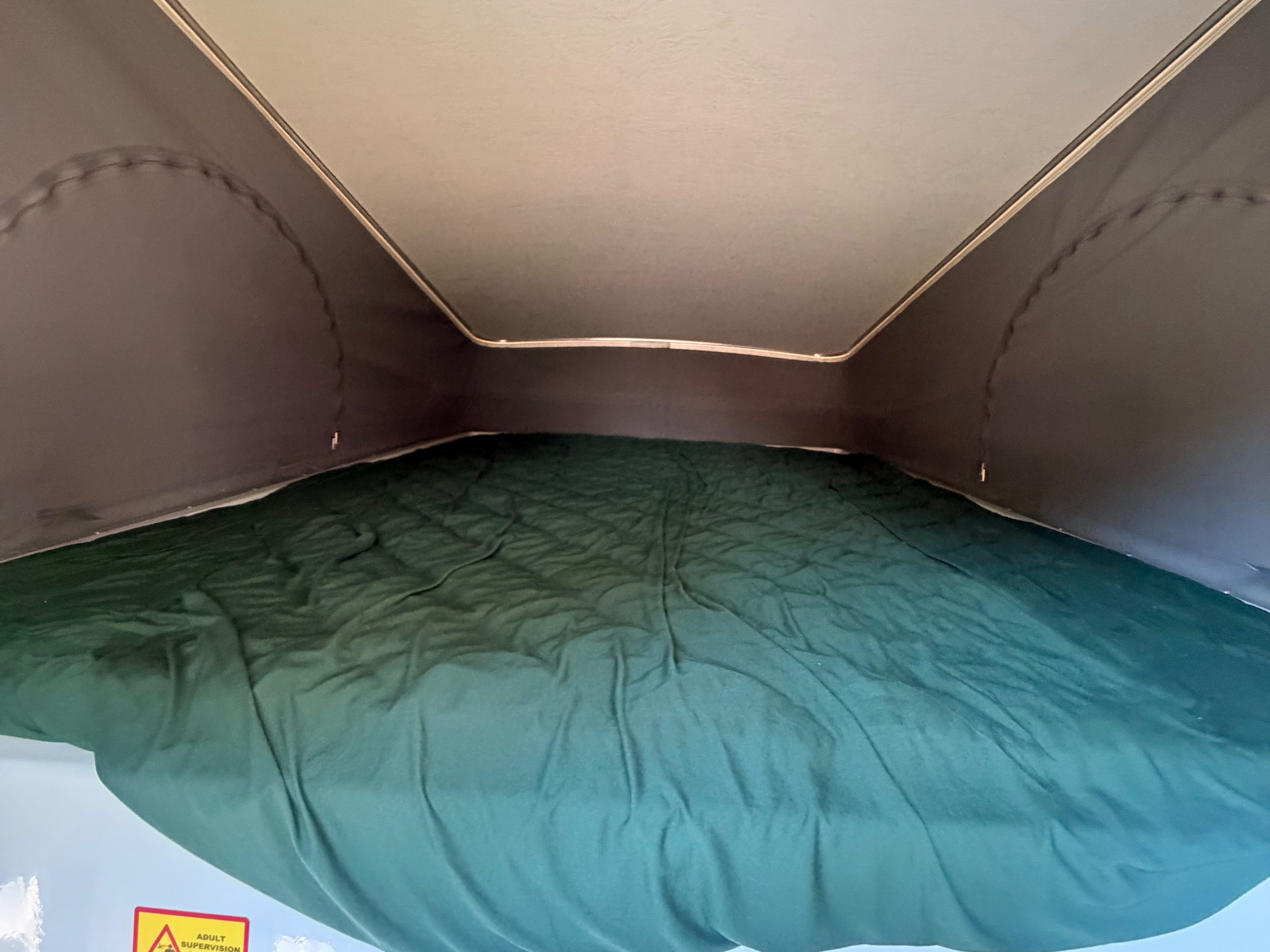 Inside an RV rental's pop-top sleeping area, featuring a dark green sheet on the mattress.. Winnebago Winnebago 2023