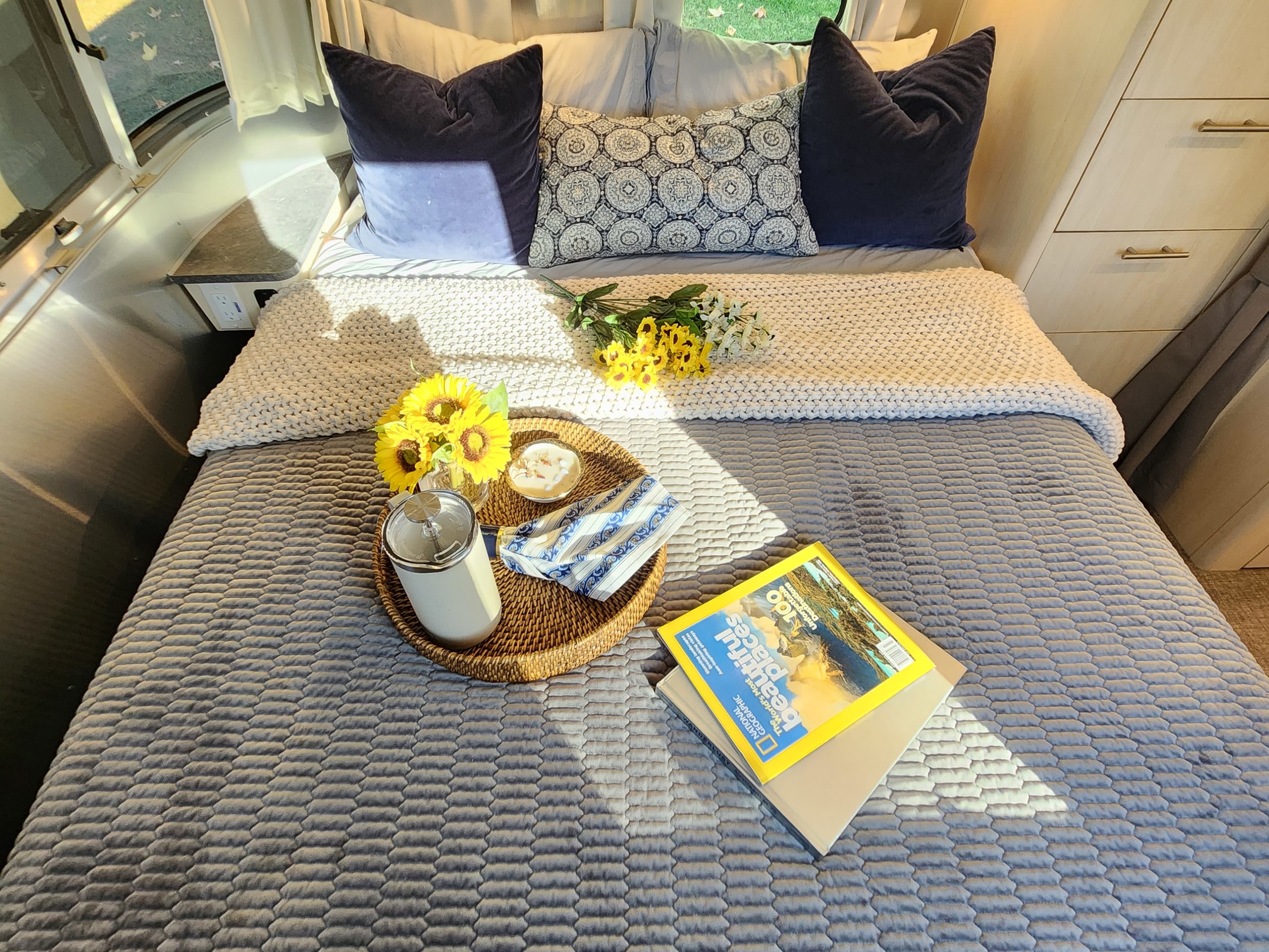 Cozy RV rental bedroom featuring a comfy bed, sunflowers, and reading materials, ready for your next adventure.. Airstream Flying Cloud 2022