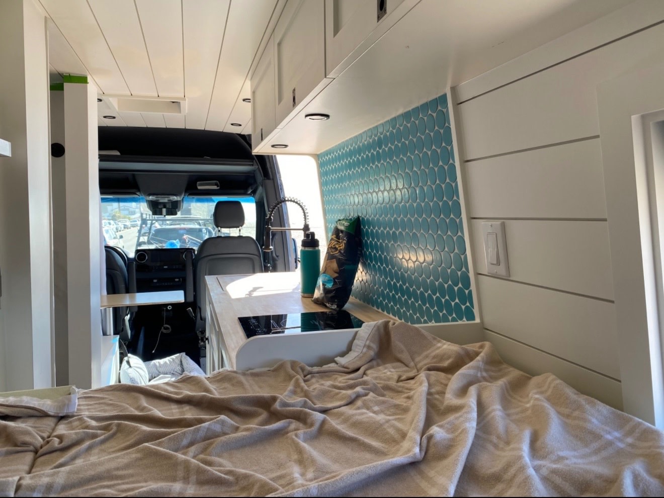 Bright camper van RV rental interior: teal tiled kitchen, cozy bed, and spacious driver's cabin visible through the back.. Mercedes-Benz Sprinter 2020