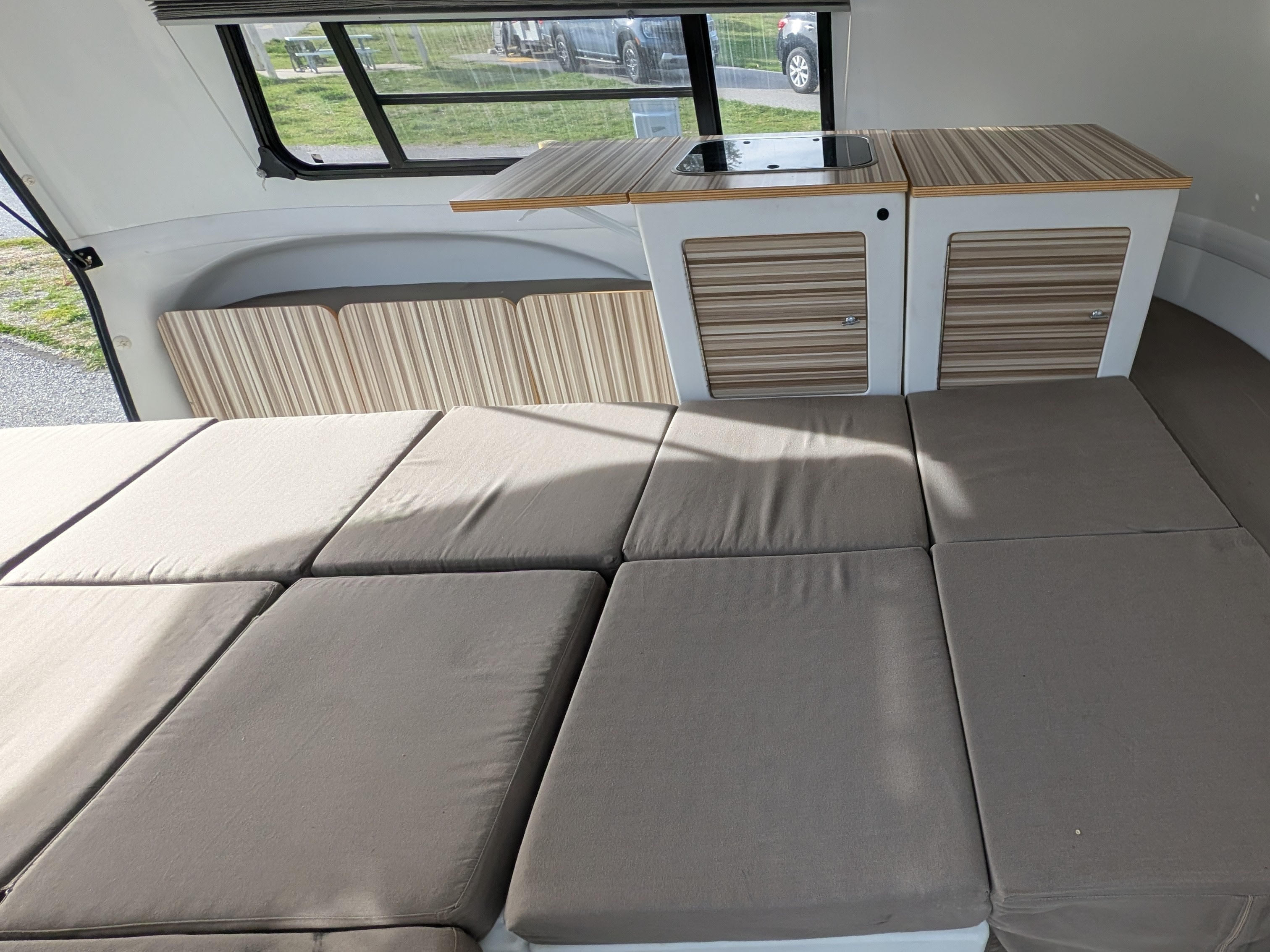 Compact RV rental interior featuring a convertible bed/seating area and a small kitchenette with striped cabinets.. Happier Camper HC1 2016
