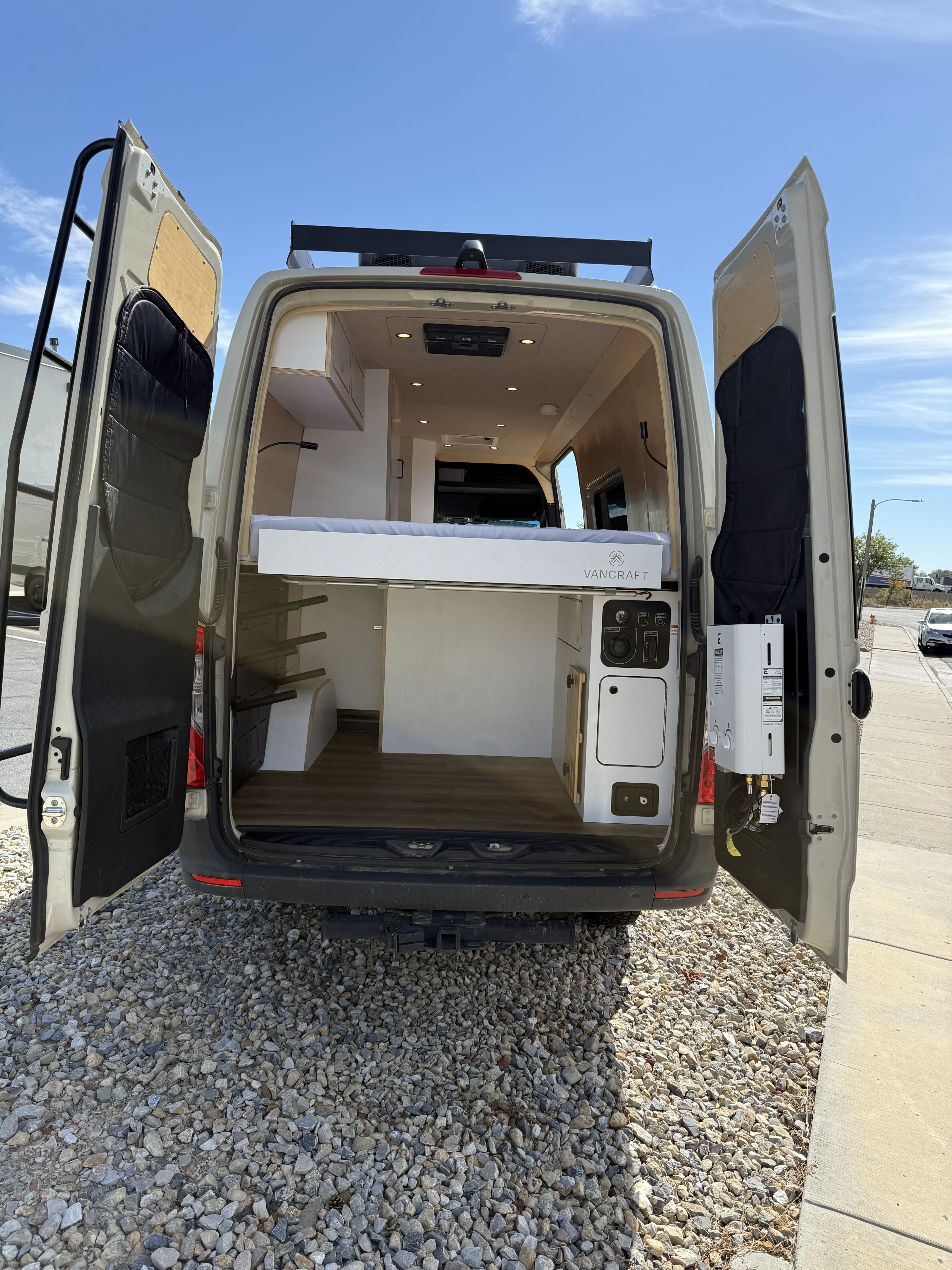 VANCRAFT RV rental camper van with open rear doors, revealing its interior bed, kitchenette, and exterior water heater.. VanCraft Other 2025