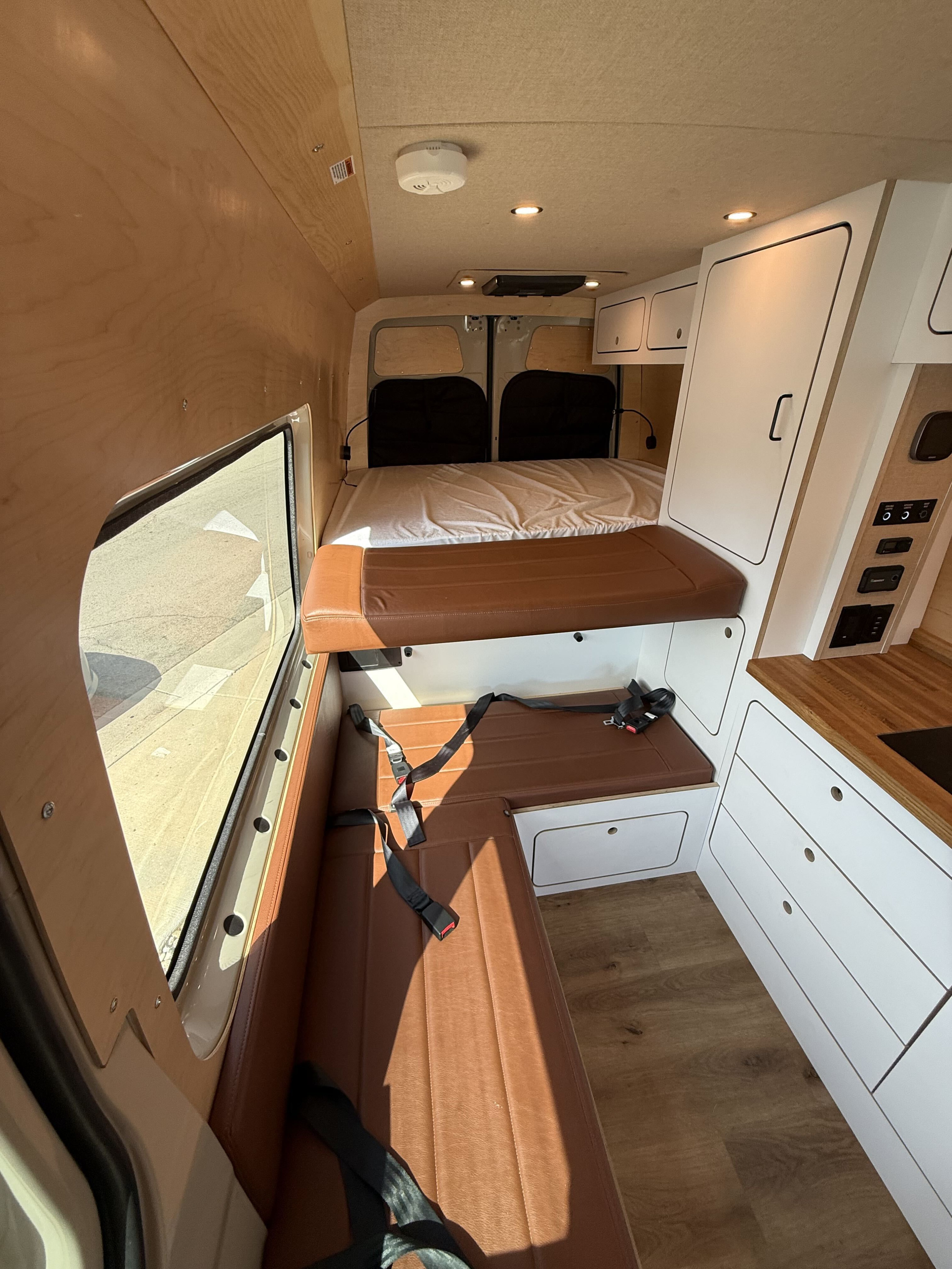 Cozy rv rental interior: comfortable bed, brown leather dinette with seatbelts, and a compact kitchen unit.. VanCraft Other 2025