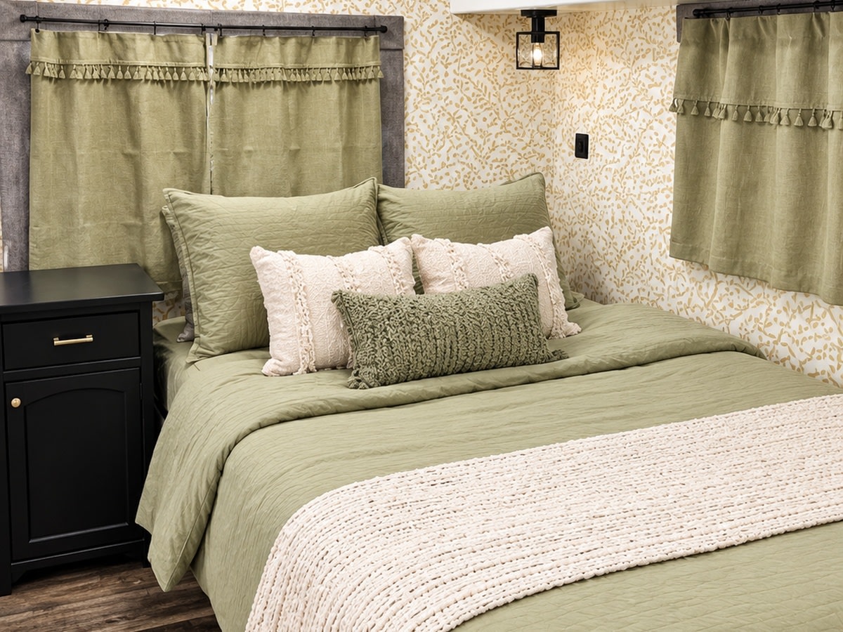 Cozy sage green bedroom in an RV rental, featuring quilted bedding, textured pillows, and leaf-patterned walls.. Coachman Mirada 2011
