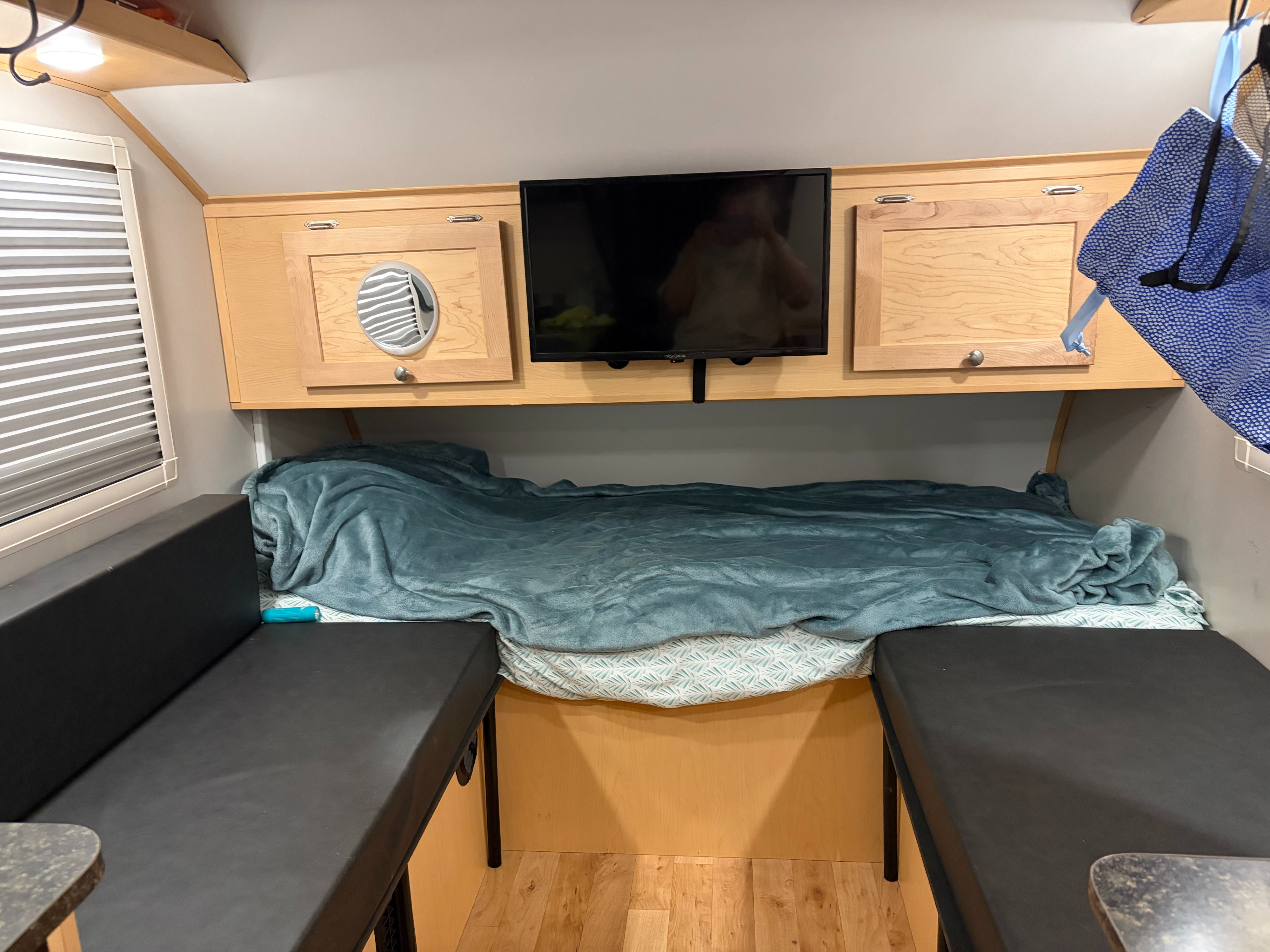 Inside an rv rental: a cozy bed with teal blanket, black cushioned seating, wooden cabinets, and a TV screen.. A Liner Grand Ascape 2023
