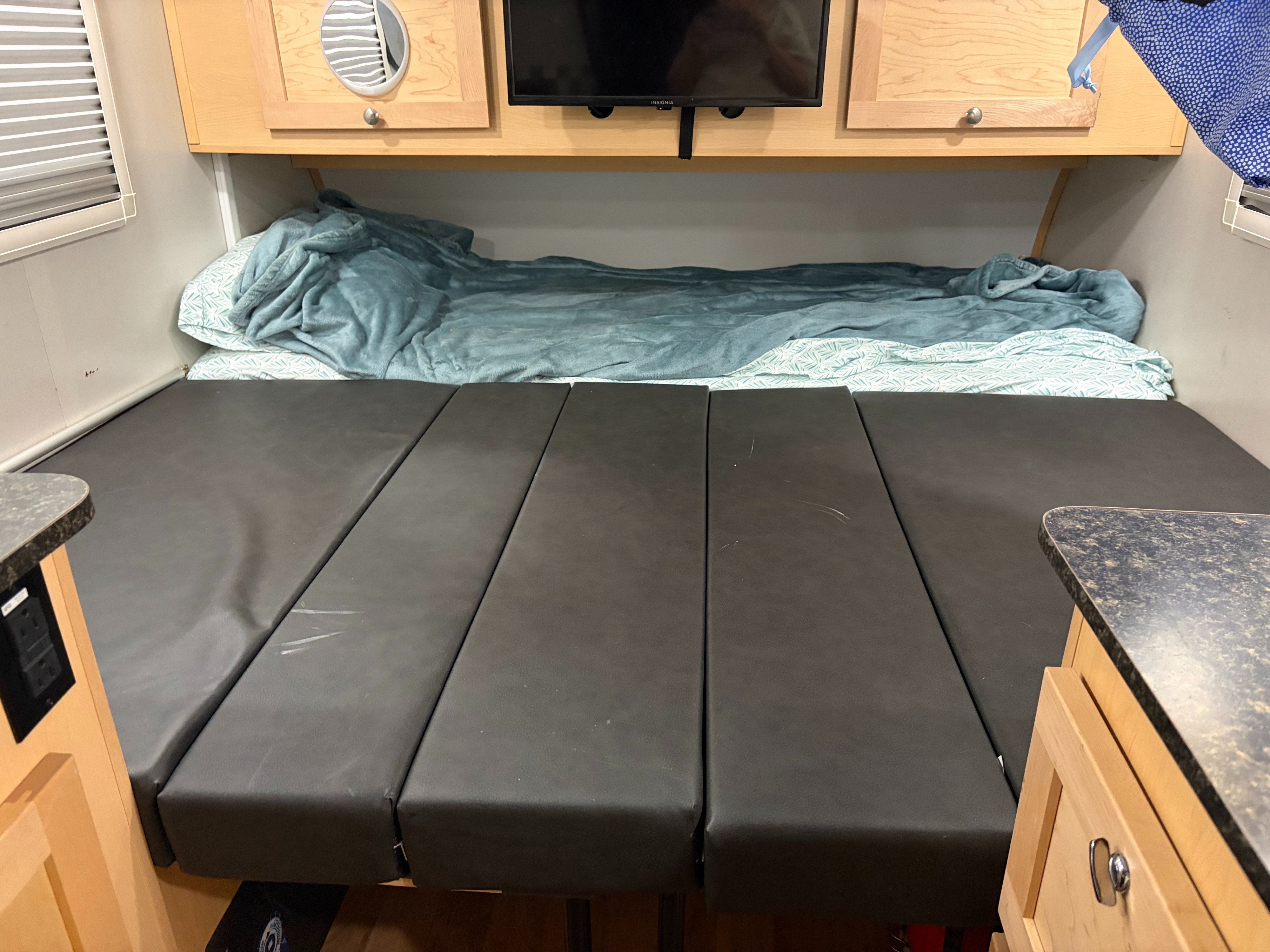 RV rental: Cozy camper interior featuring a bed with blankets, dark gray seating area, upper cabinets, and TV.. A Liner Grand Ascape 2023