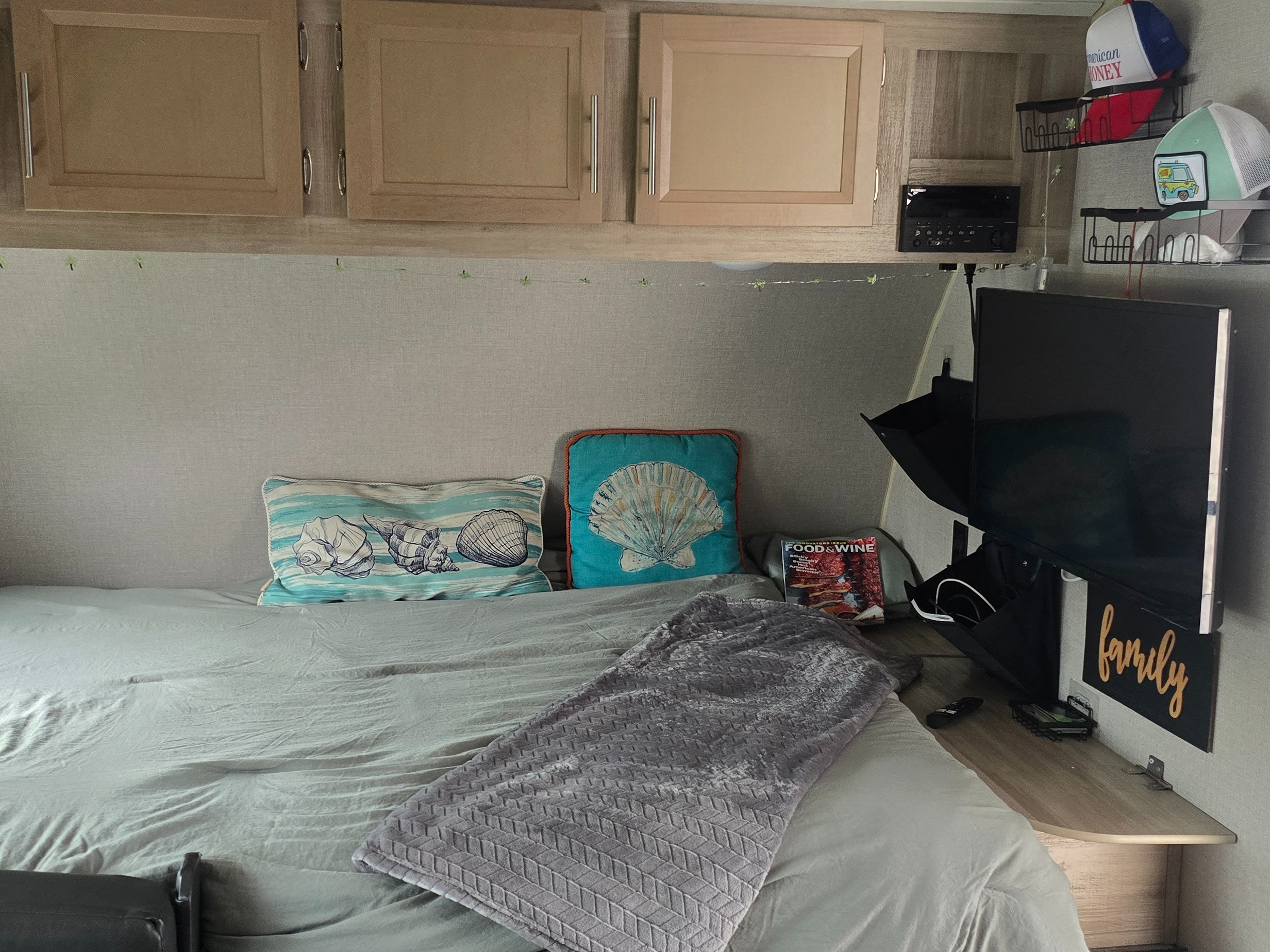 Inside a comfortable RV rental bedroom featuring a bed with seashell pillows, wall-mounted TV, and cabinets.. Coachmen Catalina 2020