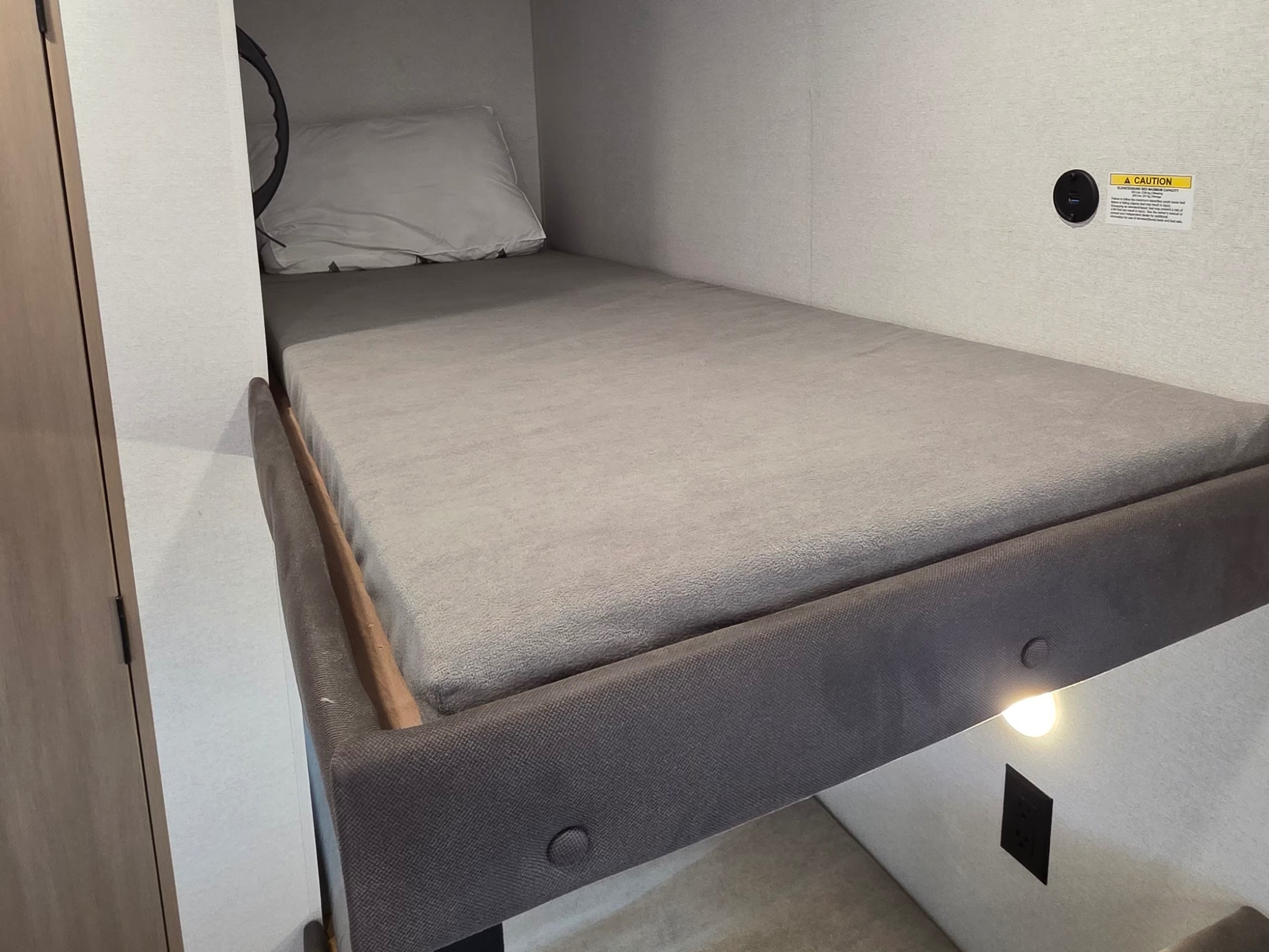 Cozy bunk bed in an RV rental, featuring a comfortable mattress, pillow, reading light, and USB charging port.. Jayco Jay Flight 2027