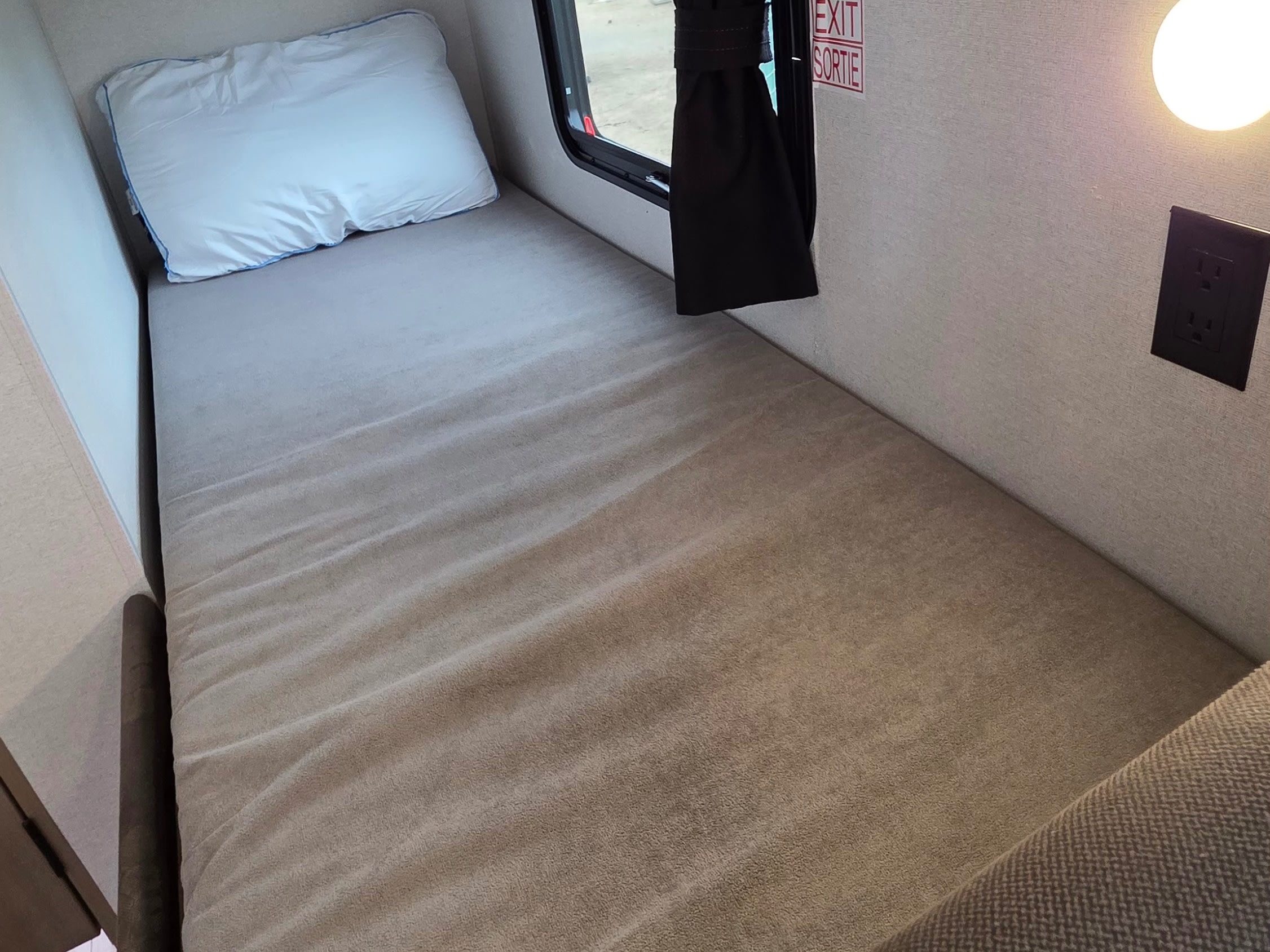 RV rental bunk bed: A narrow sleeping space with pillow, window, and power outlet, ideal for compact travel.. Jayco Jay Flight 2027
