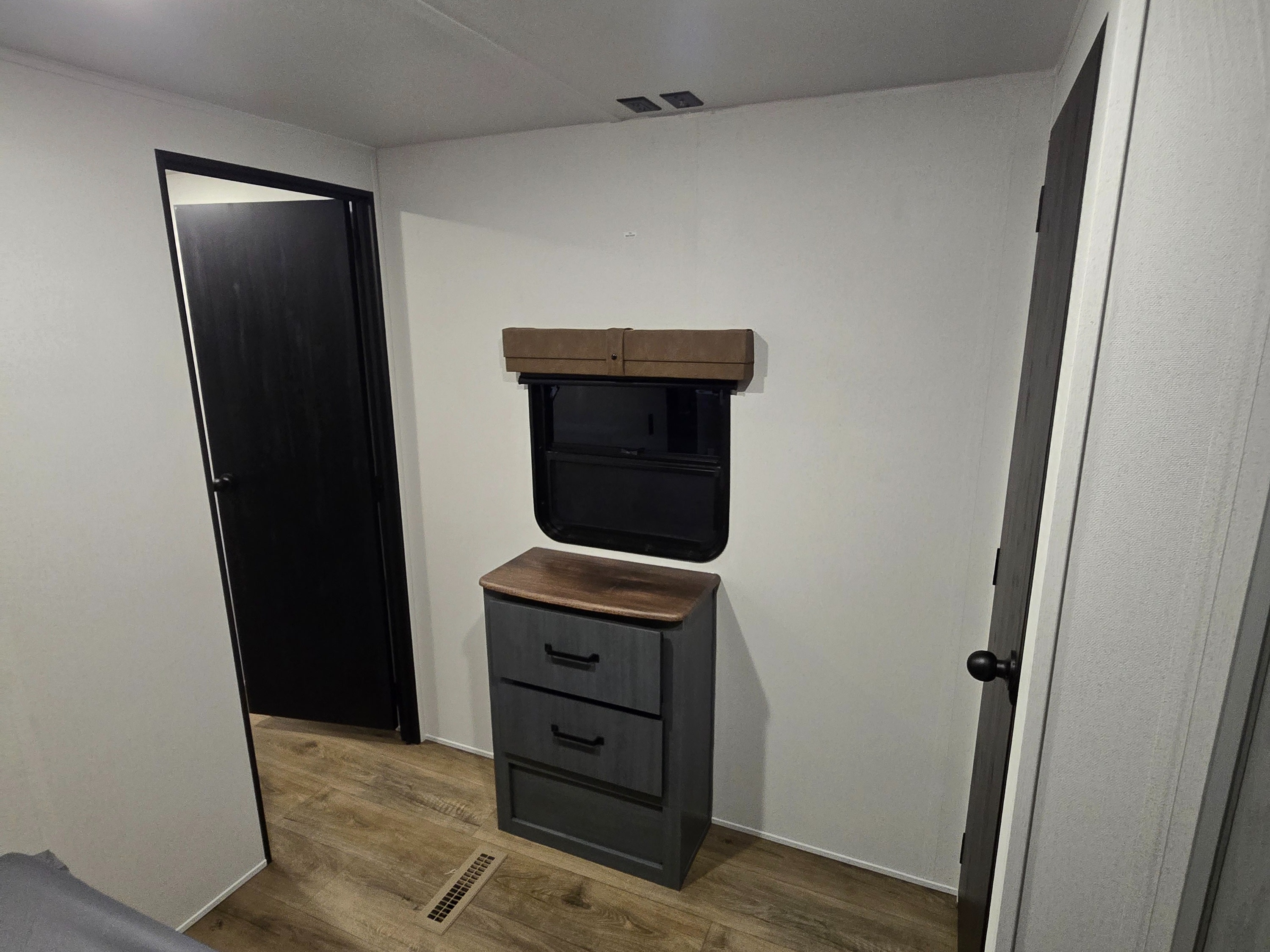 Inside an RV rental: a bedroom area with a wooden dresser, window, and two dark doors for a compact, functional space.. Forest River Puma 32bhqs 2027