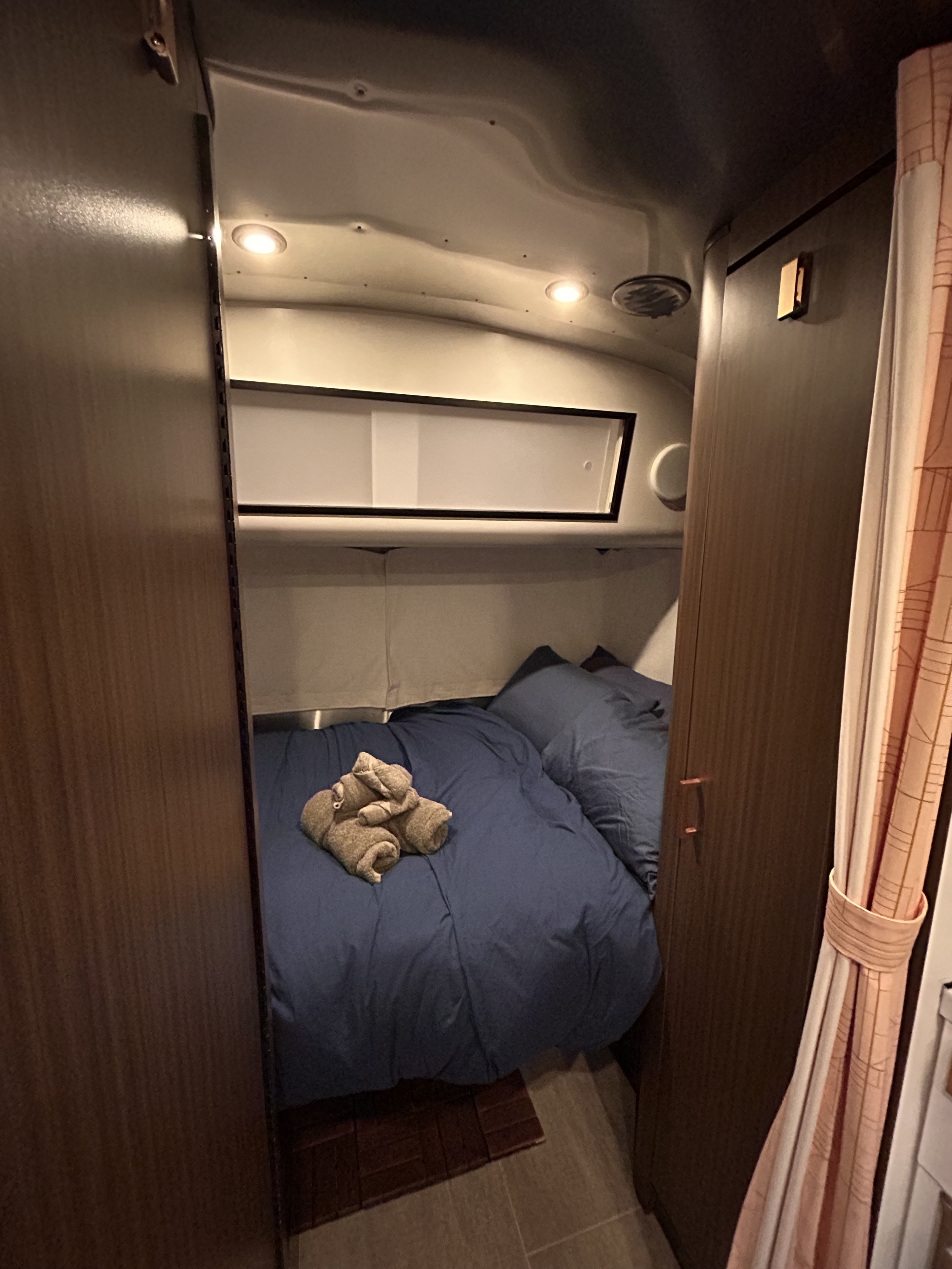 Cozy RV rental bedroom featuring a bed with blue bedding, decorative towels, and compact storage, perfect for travel.. Airstream sport 2019