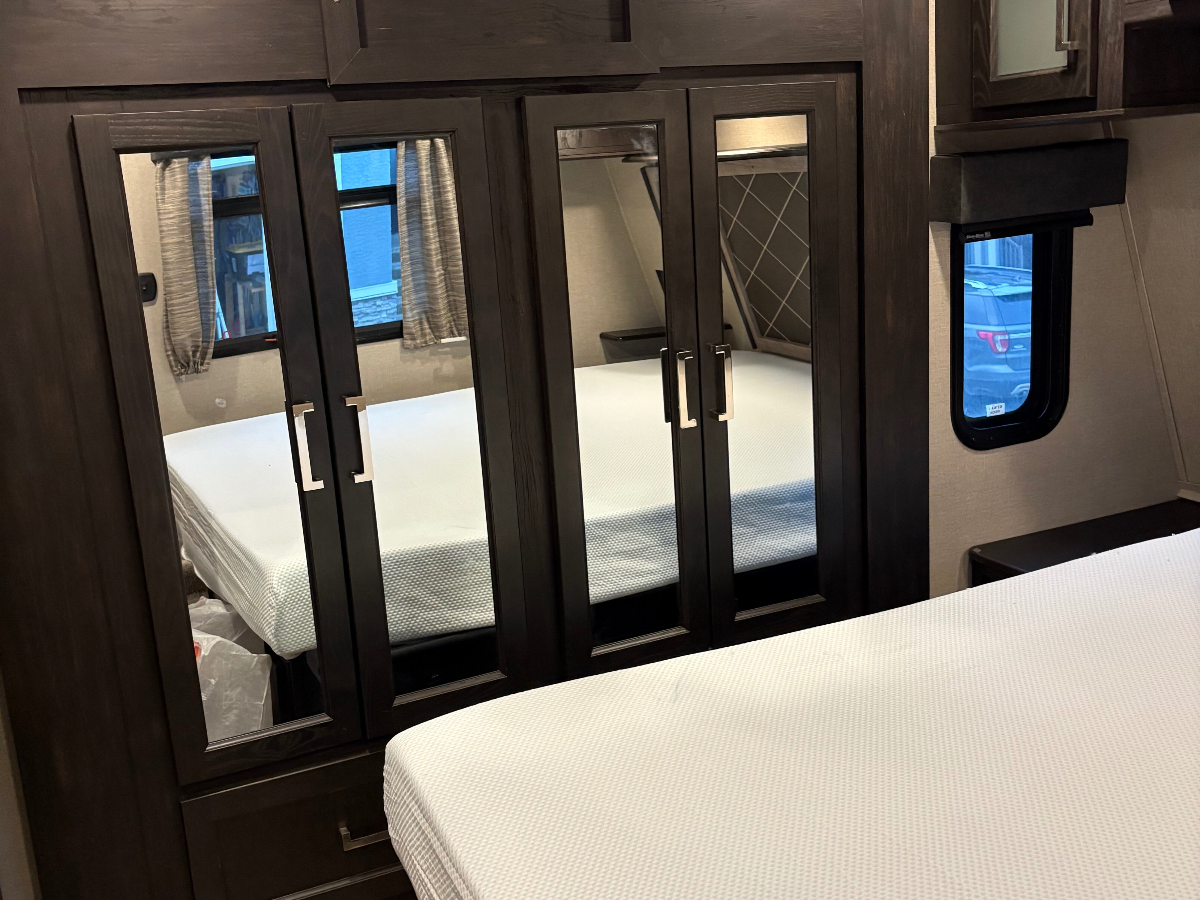 RV rental bedroom with a dark wood mirrored wardrobe reflecting the white mattress and interior space.. Keystone Fuzion 2019