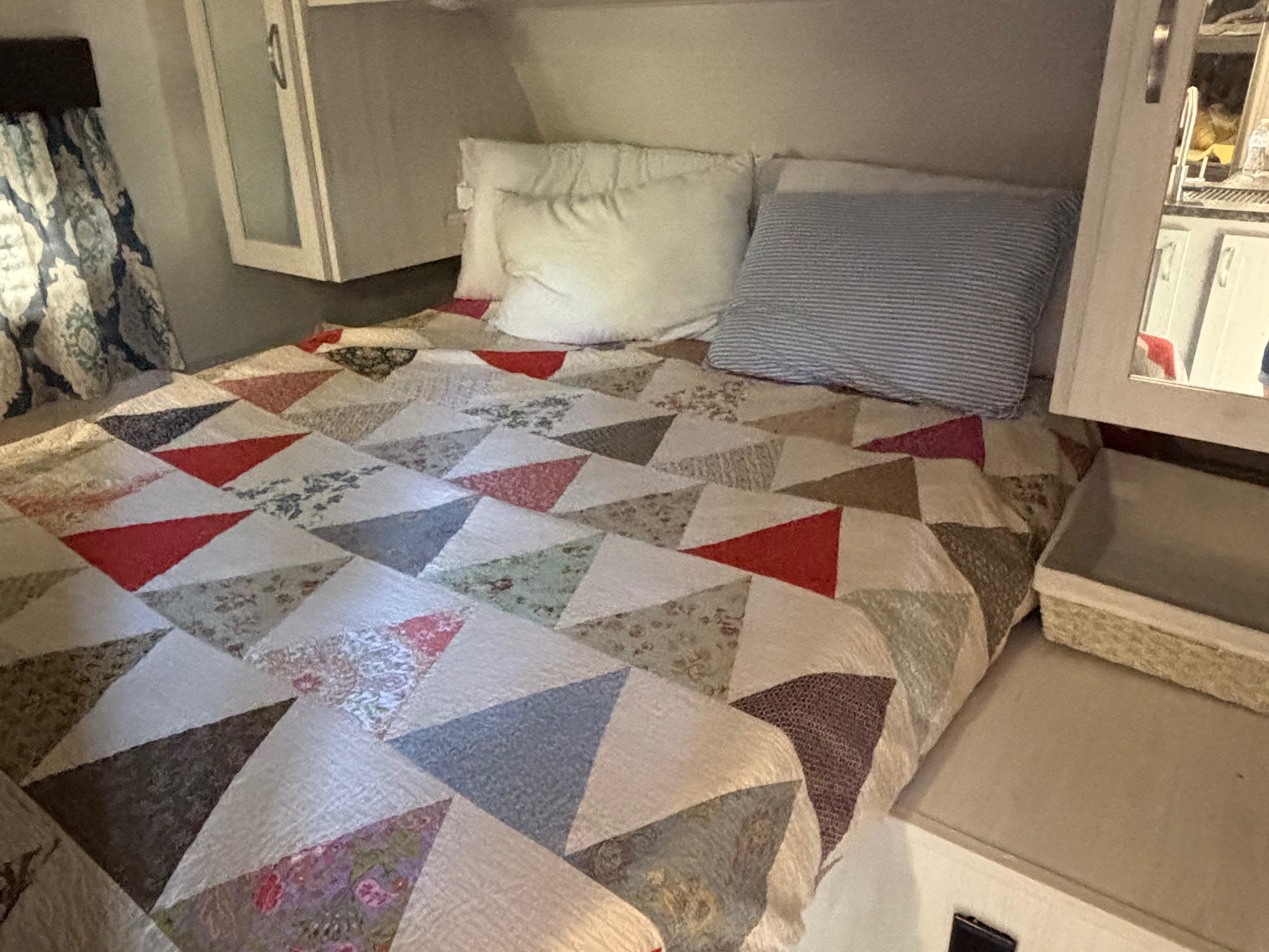 This RV rental bedroom offers a cozy bed with a colorful patchwork quilt, two pillows, and handy overhead storage.. Forest River Tracer 2021