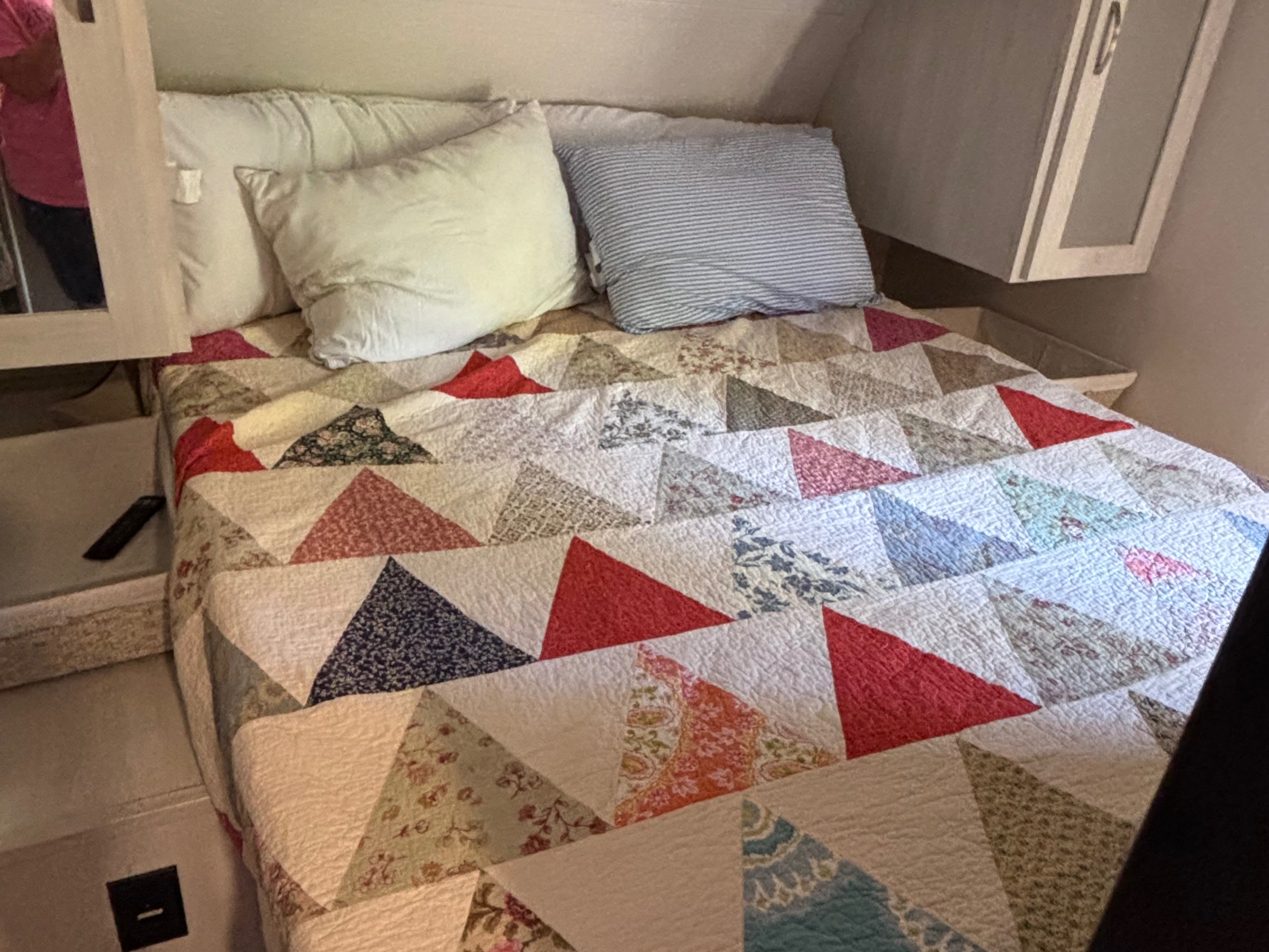 This RV rental bedroom features a comfy bed with a vibrant patchwork quilt, pillows, and overhead storage for a cozy stay.. Forest River Tracer 2021