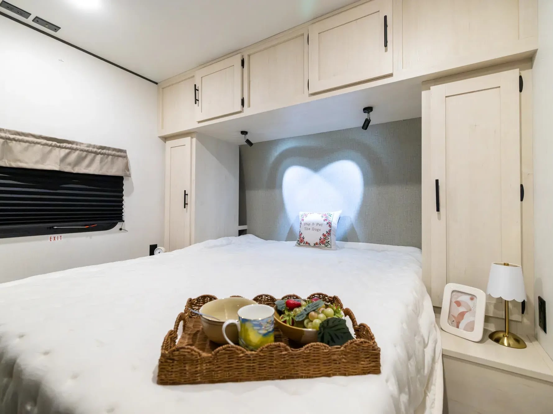 Cozy RV rental bedroom with breakfast in bed, heart-shaped light, overhead storage, and an exit window.. Coachmen Shasta 2027