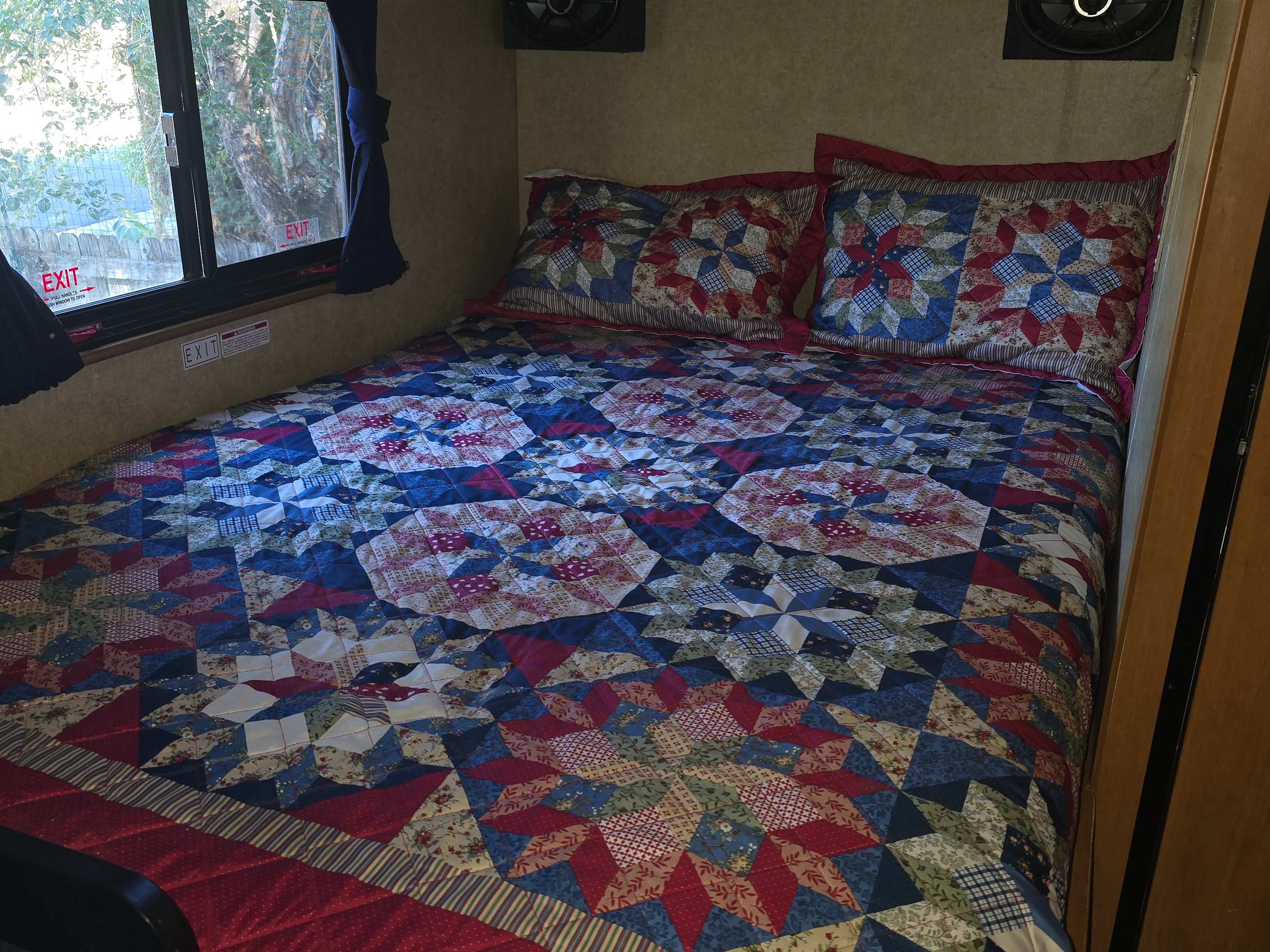 Cozy RV rental bedroom with a colorful star-patterned quilt and matching pillows, featuring an emergency exit window.. Thor Motor Coach Four Winds Majestic 2015