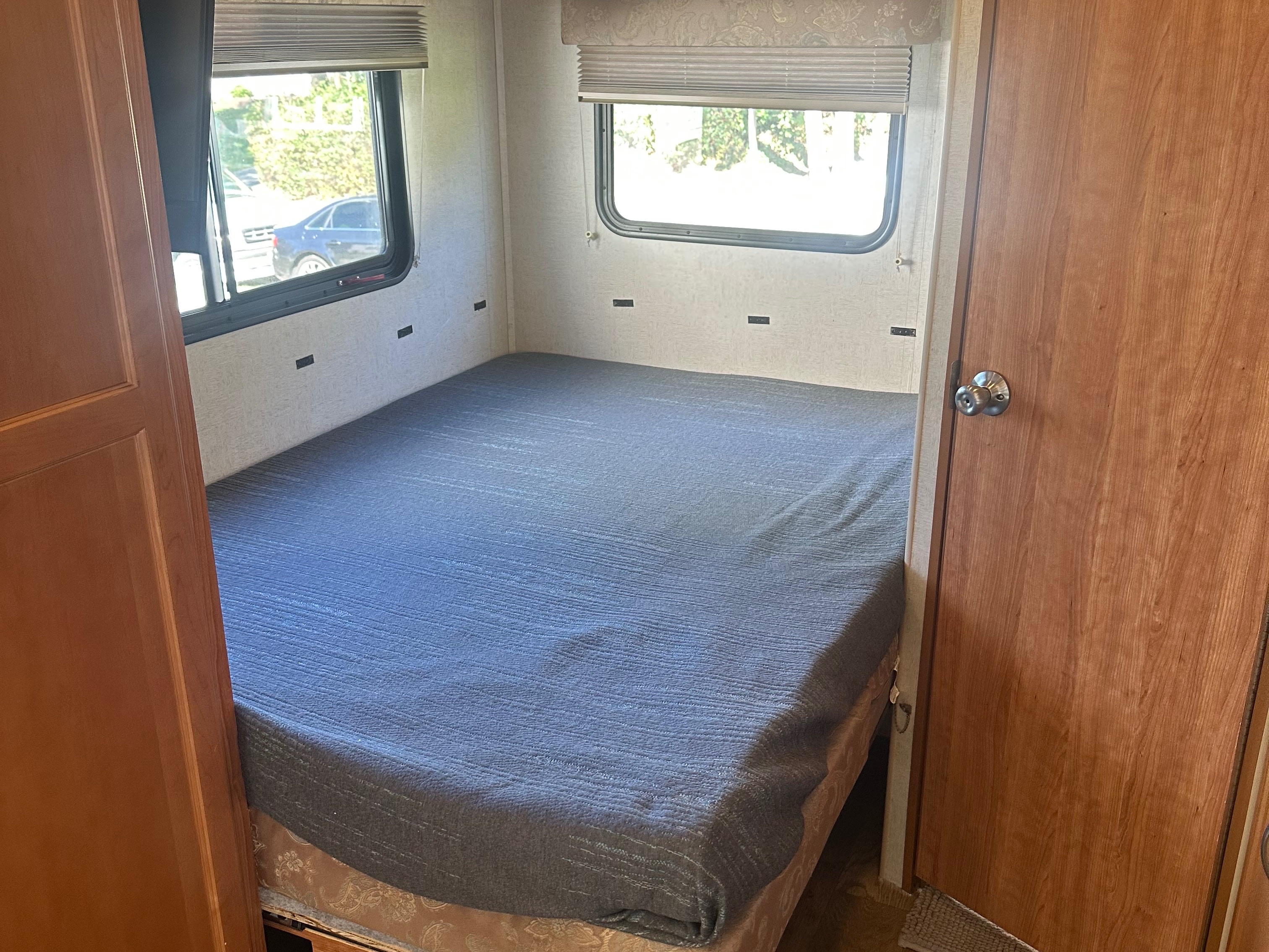 Interior of an RV rental bedroom: features a neatly made bed, two windows with blinds, and light wooden doors.. Fleetwood Other 2010