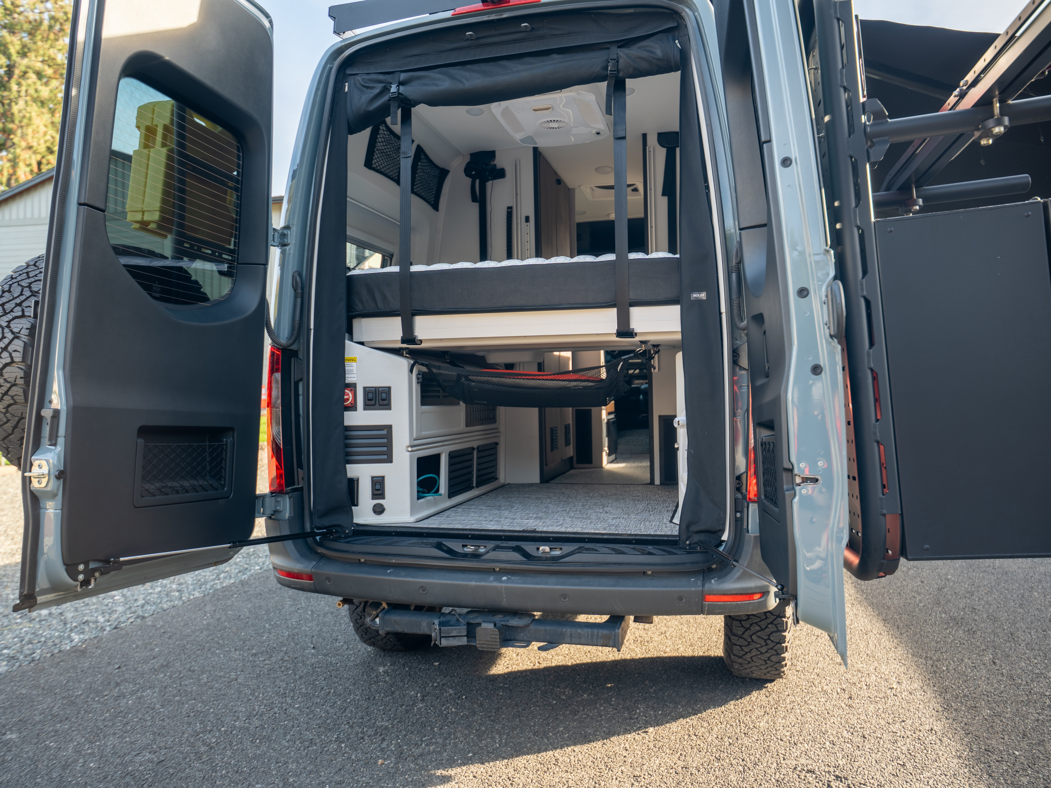 Explore this RV rental's spacious camper van interior! Rear view shows a raised bed, storage, and custom features for adventure.. Tiffin Motorhomes GH1 2025