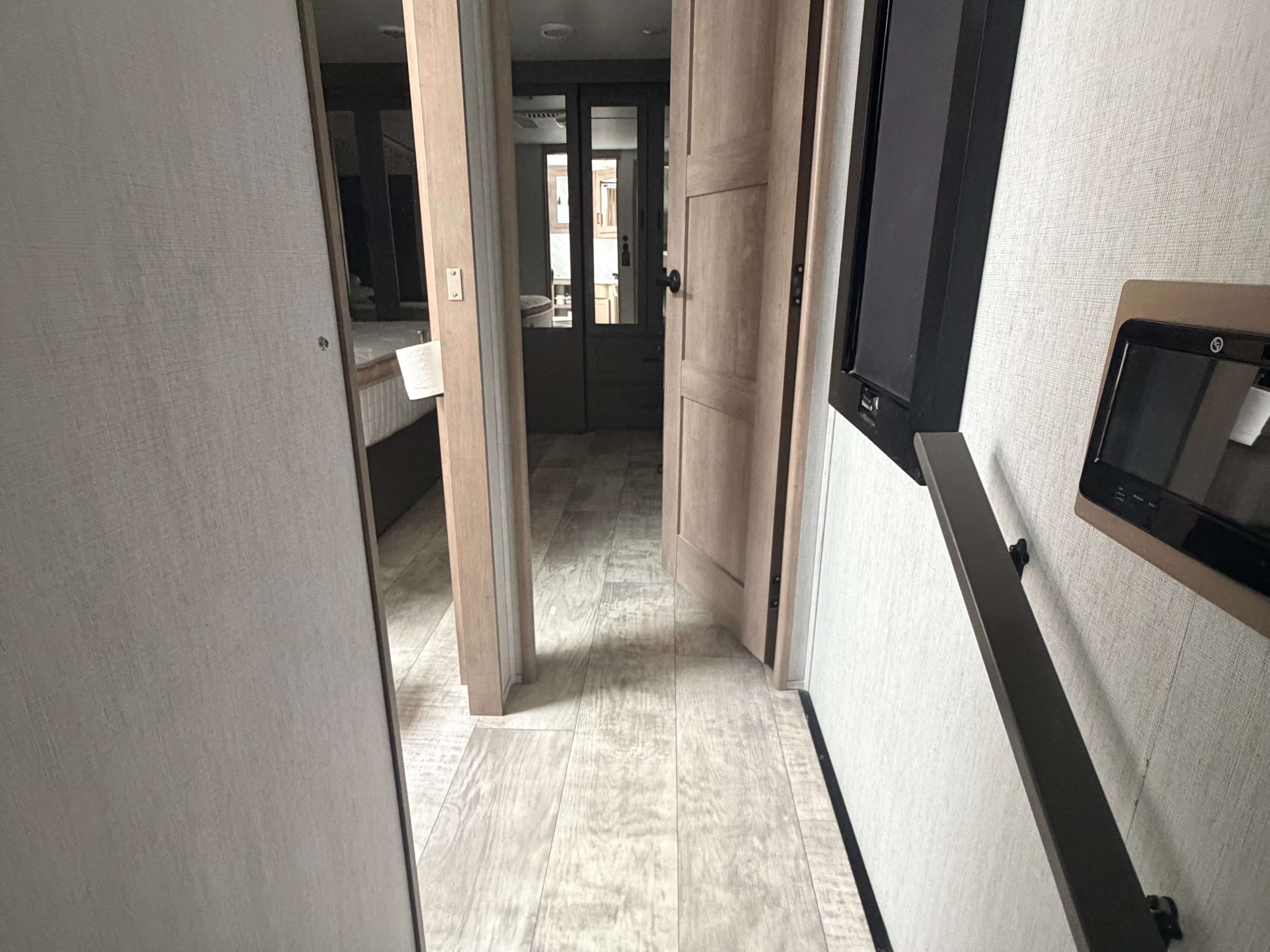 RV rental interior: A hallway with light wood flooring, open doors to a bedroom & living area, and a wall-mounted screen/handrail.. Grand Design Momentum M-Class Toy Hauler 2023