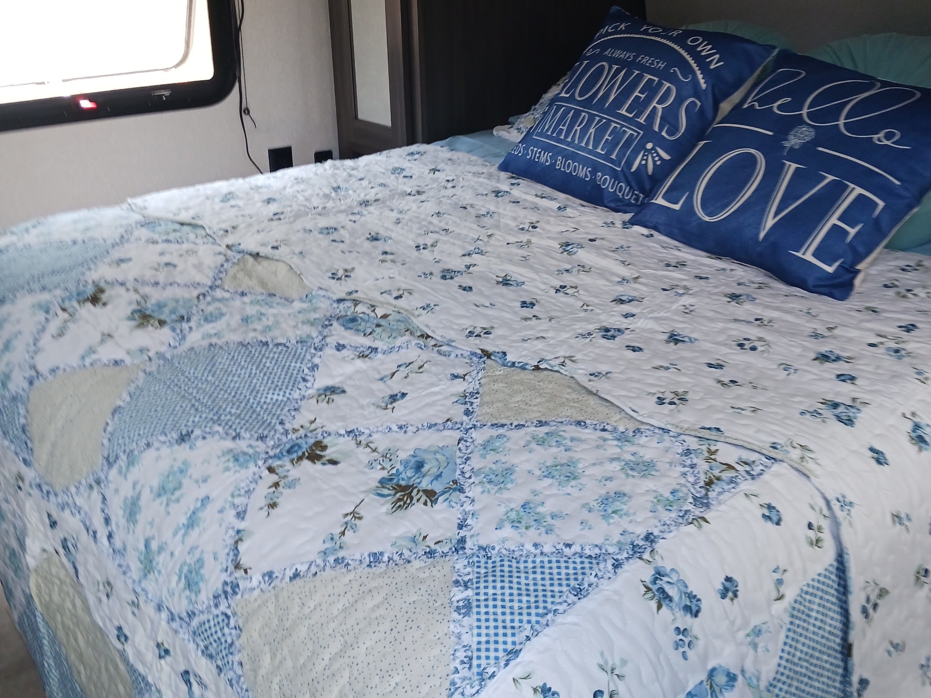 Cozy RV rental bedroom featuring a bed with a blue and white floral quilt and decorative pillows.. Forest River Shasta 2021