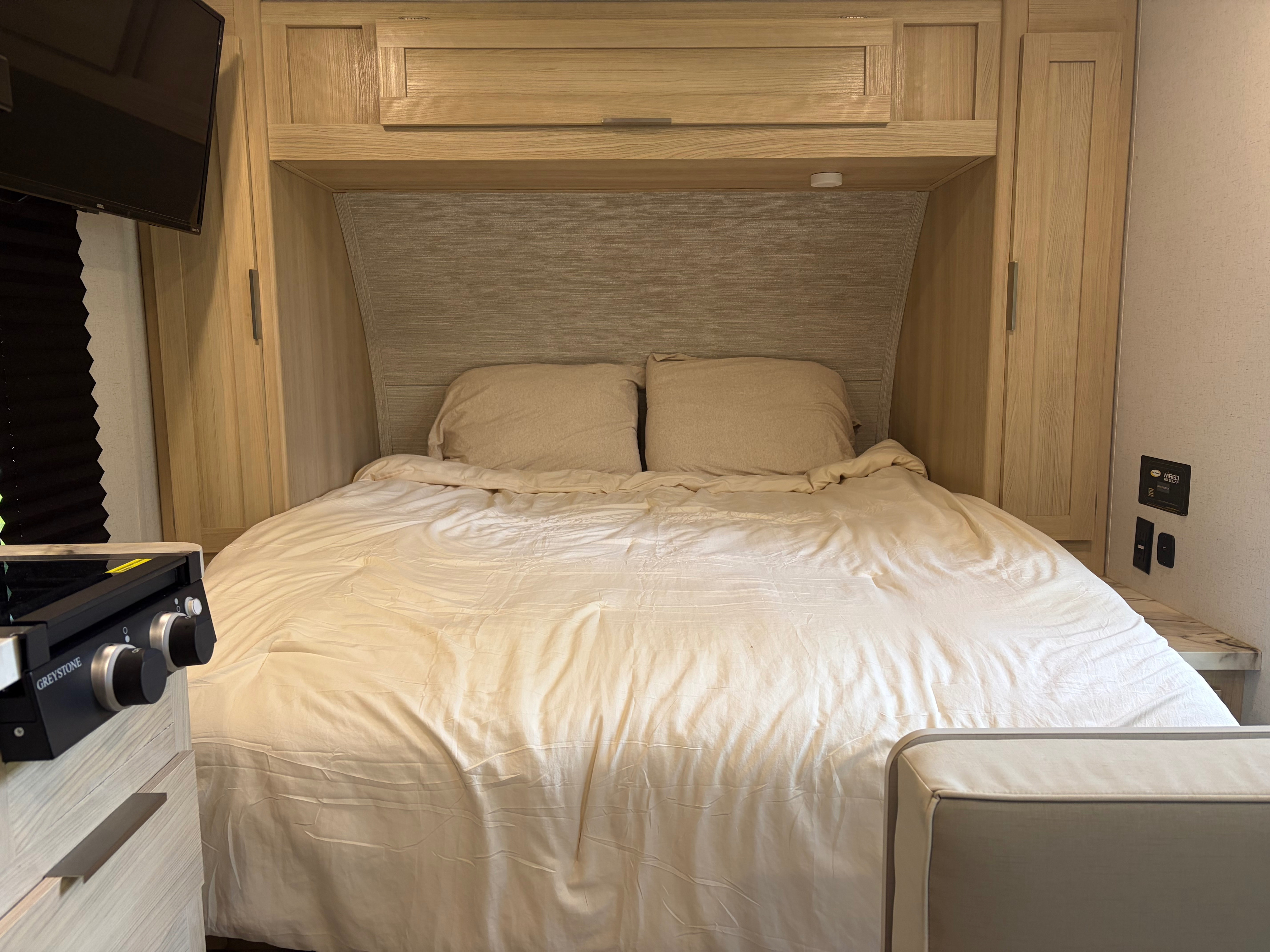 Compact RV rental bedroom featuring a full bed, overhead storage, and a built-in Greystone cooktop for versatile living.. Forest River Wildwood FSX Platinum 2023