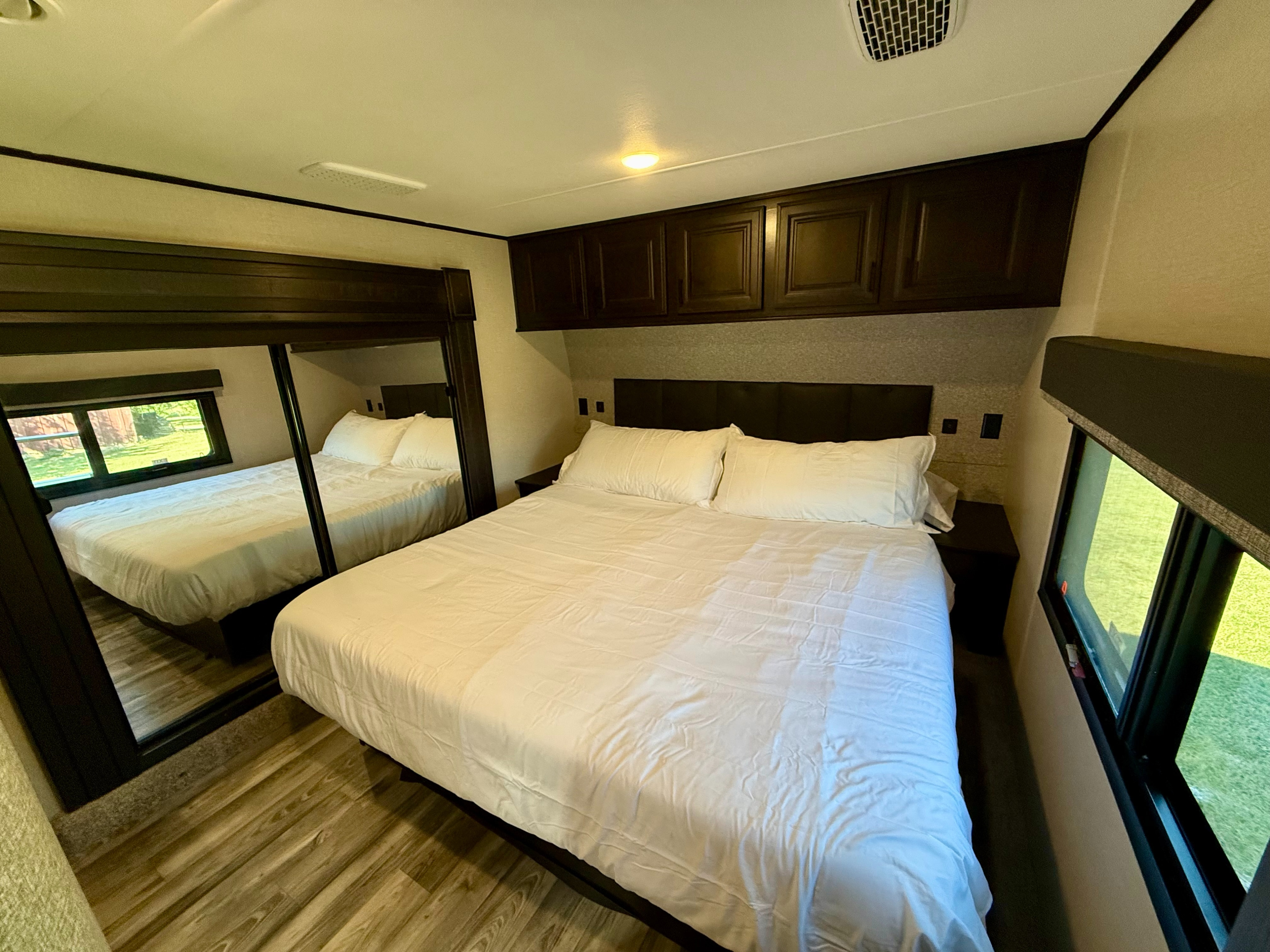 Spacious RV rental bedroom with a comfy bed, dark wood cabinets, and large mirror. Bright windows show nature outside.. Highland Ridge RV Open Range 2022