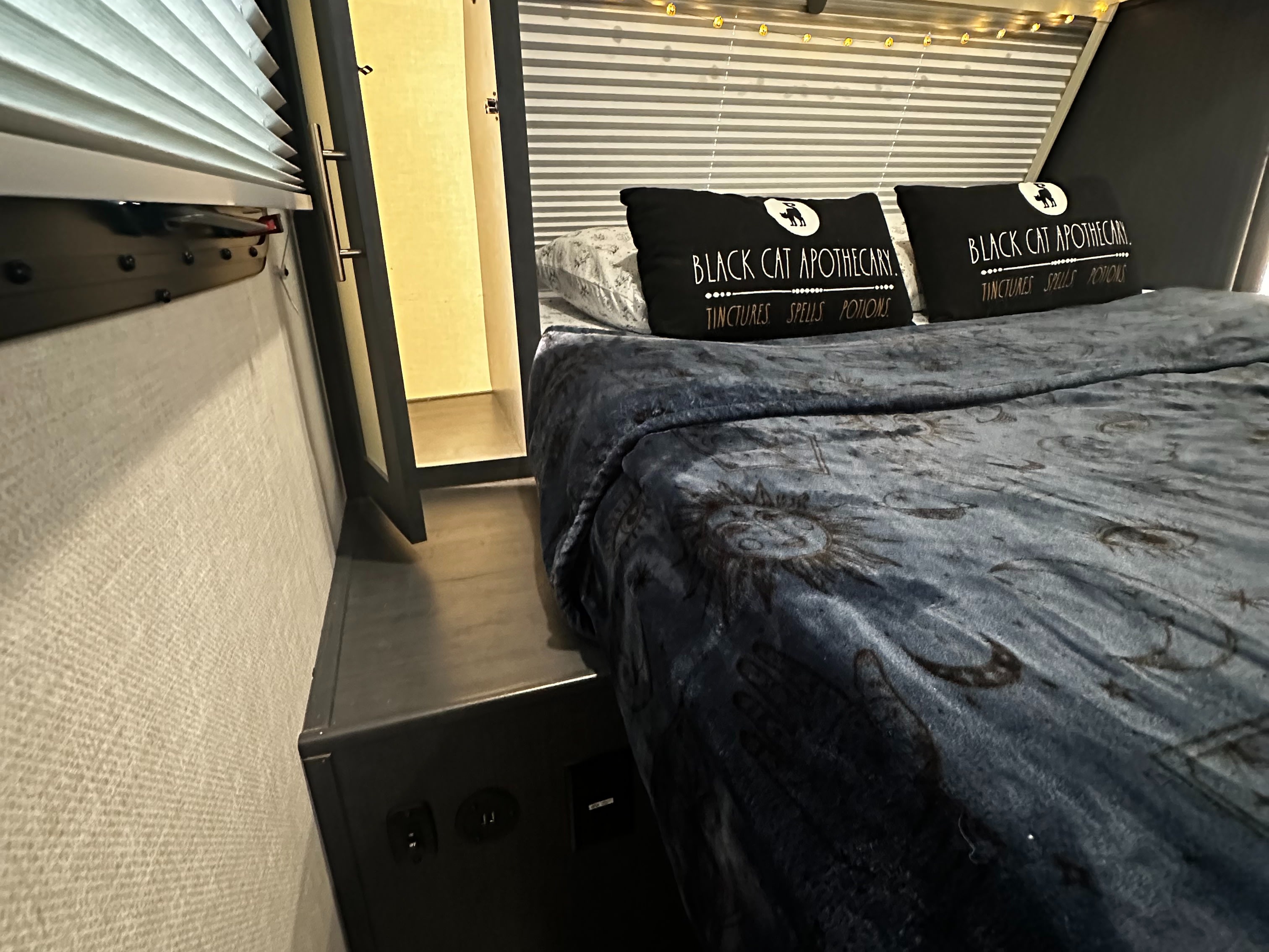 Cozy RV rental bedroom with "Black Cat Apothecary" pillows and a celestial blanket, illuminated by warm fairy lights.. Forest River R-Pod 202 2024