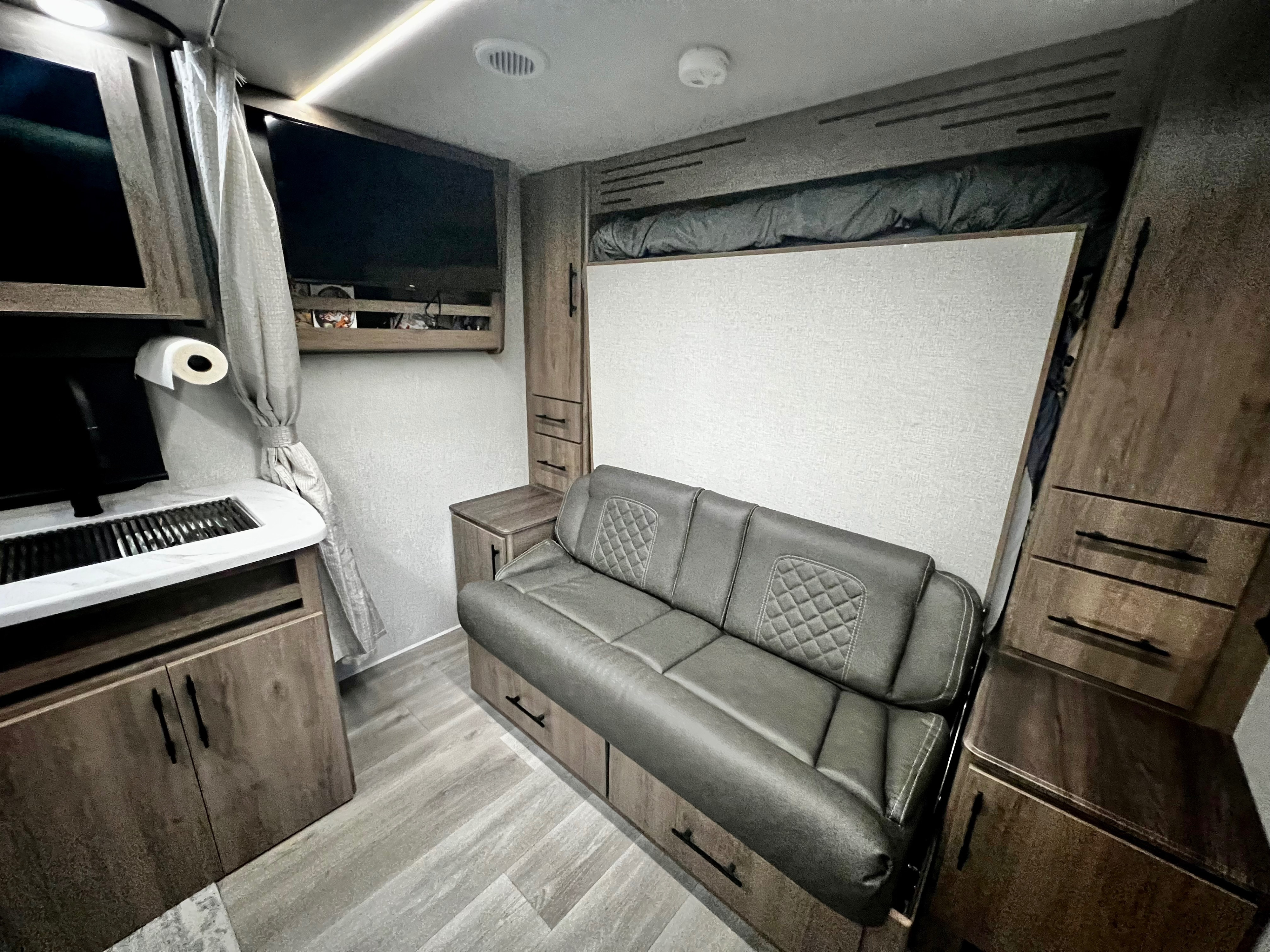 RV rental interior: gray convertible sofa, hidden murphy bed, compact kitchen, TV, and wood-look storage.. Grand Design Imagine XLS 2023