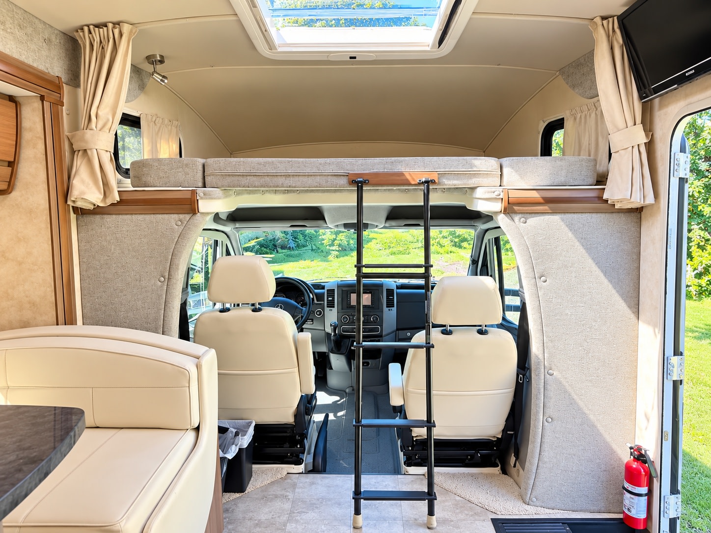 This bright rv rental interior shows an overhead bunk, ladder, driver's cabin, and dinette, offering comfort and a view outside.. Itasca Navion 2015