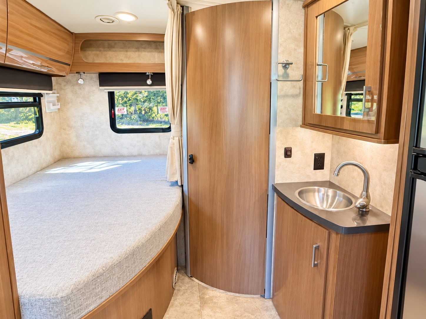 RV rental interior: comfy bed, compact sink vanity, and warm wood cabinetry. Your mobile home awaits adventure.. Itasca Navion 2015