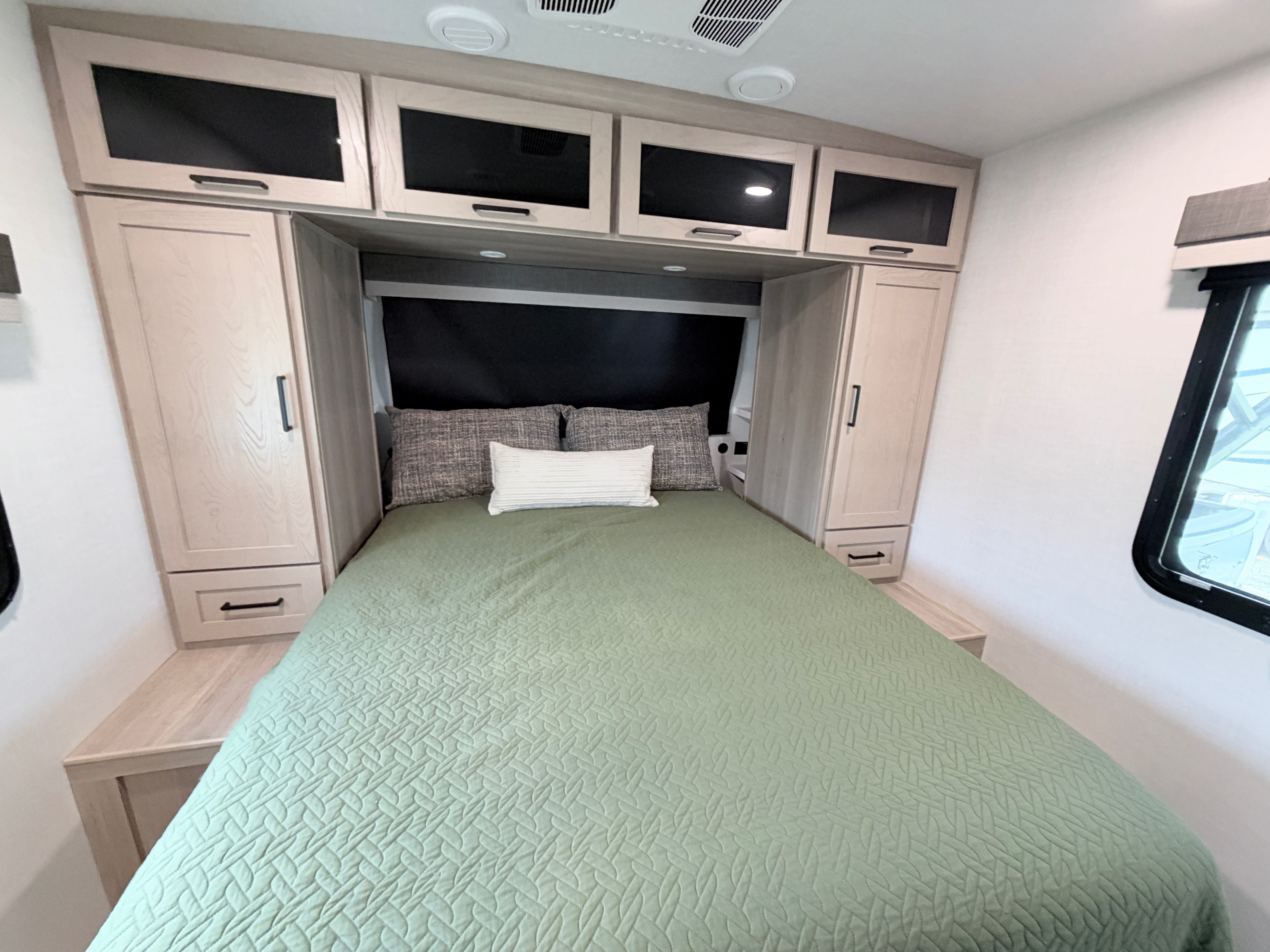 Cozy RV rental bedroom with a comfy bed, green comforter, and ample overhead and side storage cabinets for a pleasant stay.. Forest River 2706BH 2026