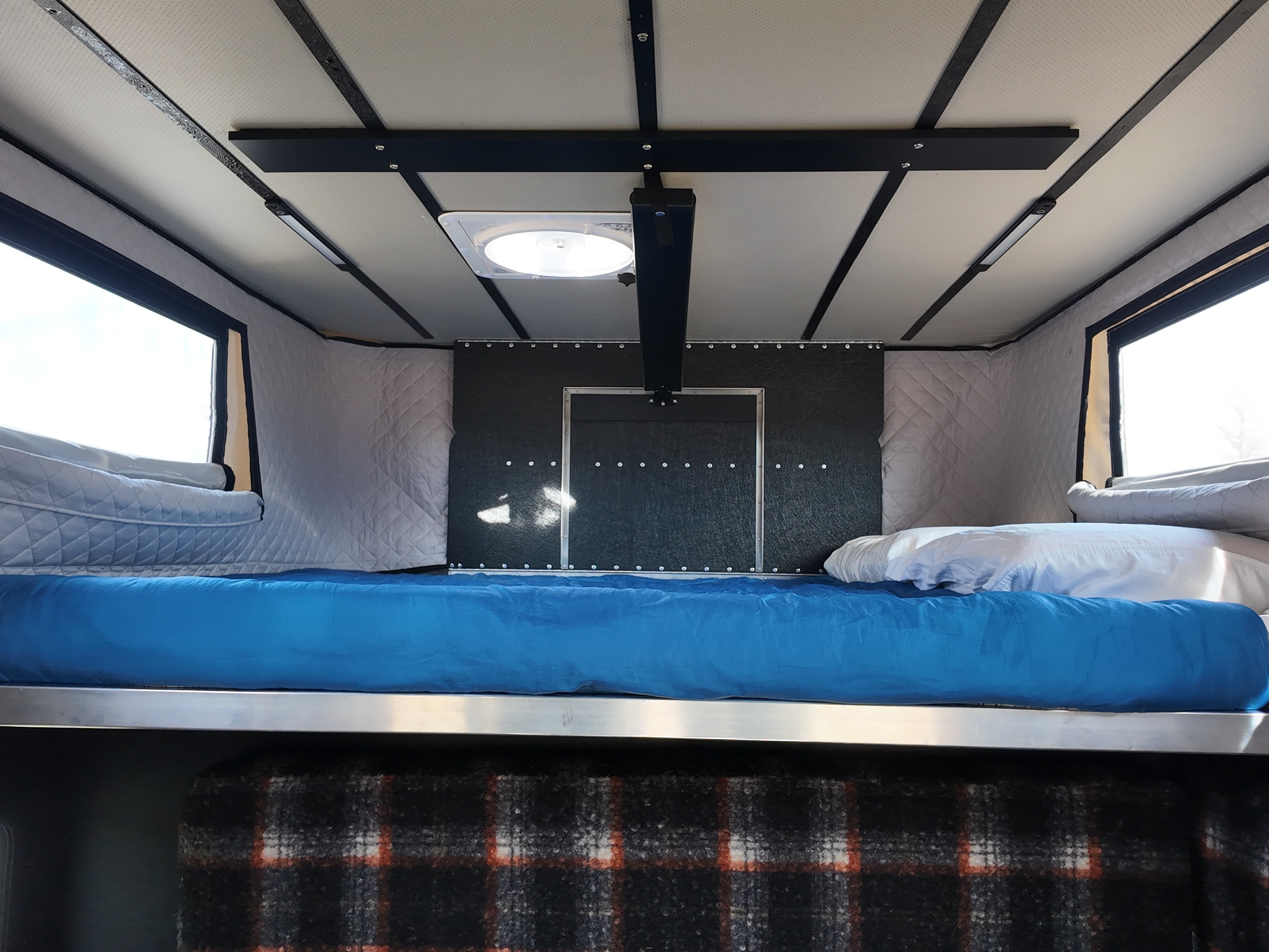 Interior of an RV rental: blue bed, white pillows, quilted grey walls, ceiling fan, & windows, offering a cozy sleeping area.. Ford F350 2025