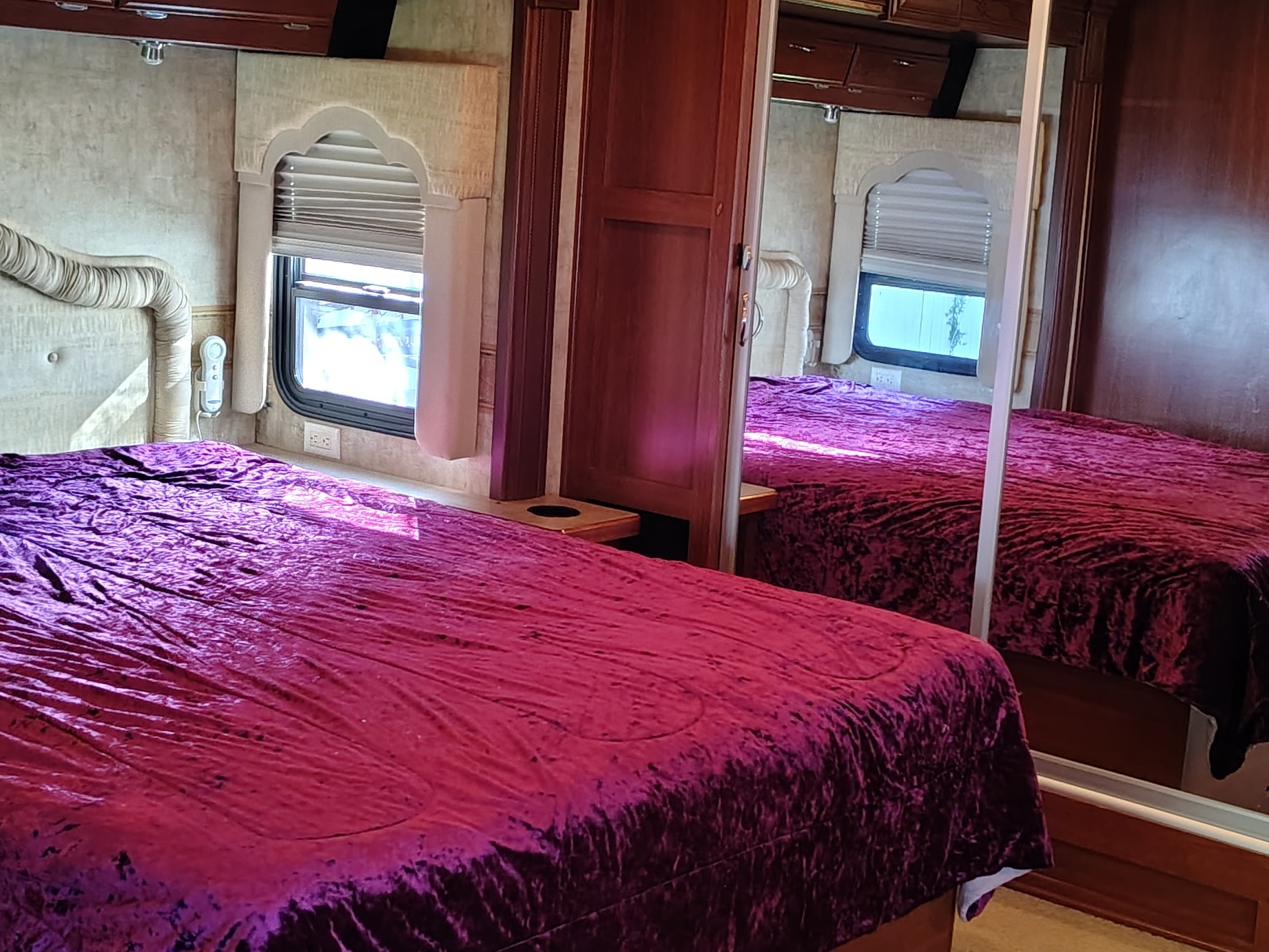 Cozy RV rental bedroom with a plush purple velvet bed, window with blinds, and mirrored wardrobe for a comfortable on-the-road stay.. Fleetwood 38v 2008
