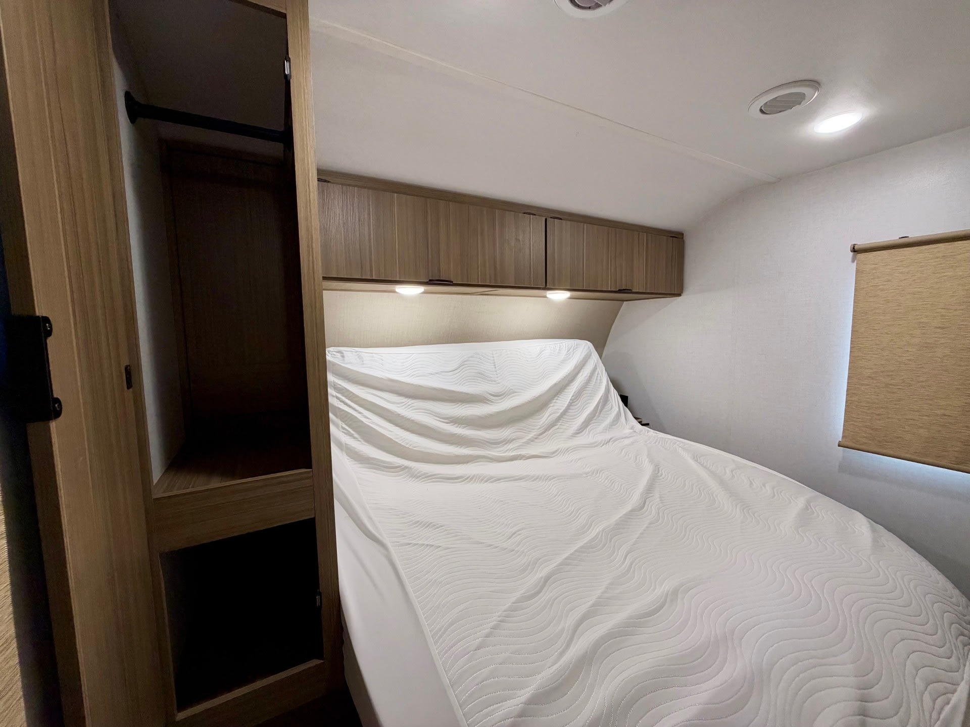 Cozy RV rental bedroom featuring a bed with white bedding, overhead storage cabinets, and a closet. Ideal for travel.. Forest River Salem View 2025