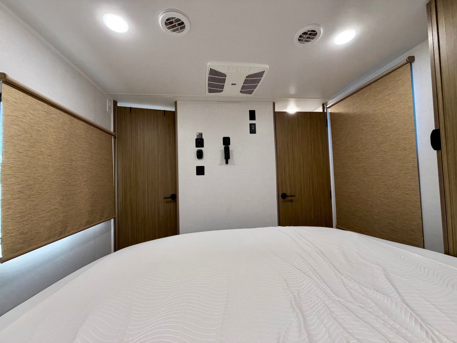 Inside a modern RV rental bedroom: crisp white bed, two windows with blinds, dual doors, ceiling lights, and integrated AC system.. Forest River Salem View 2025