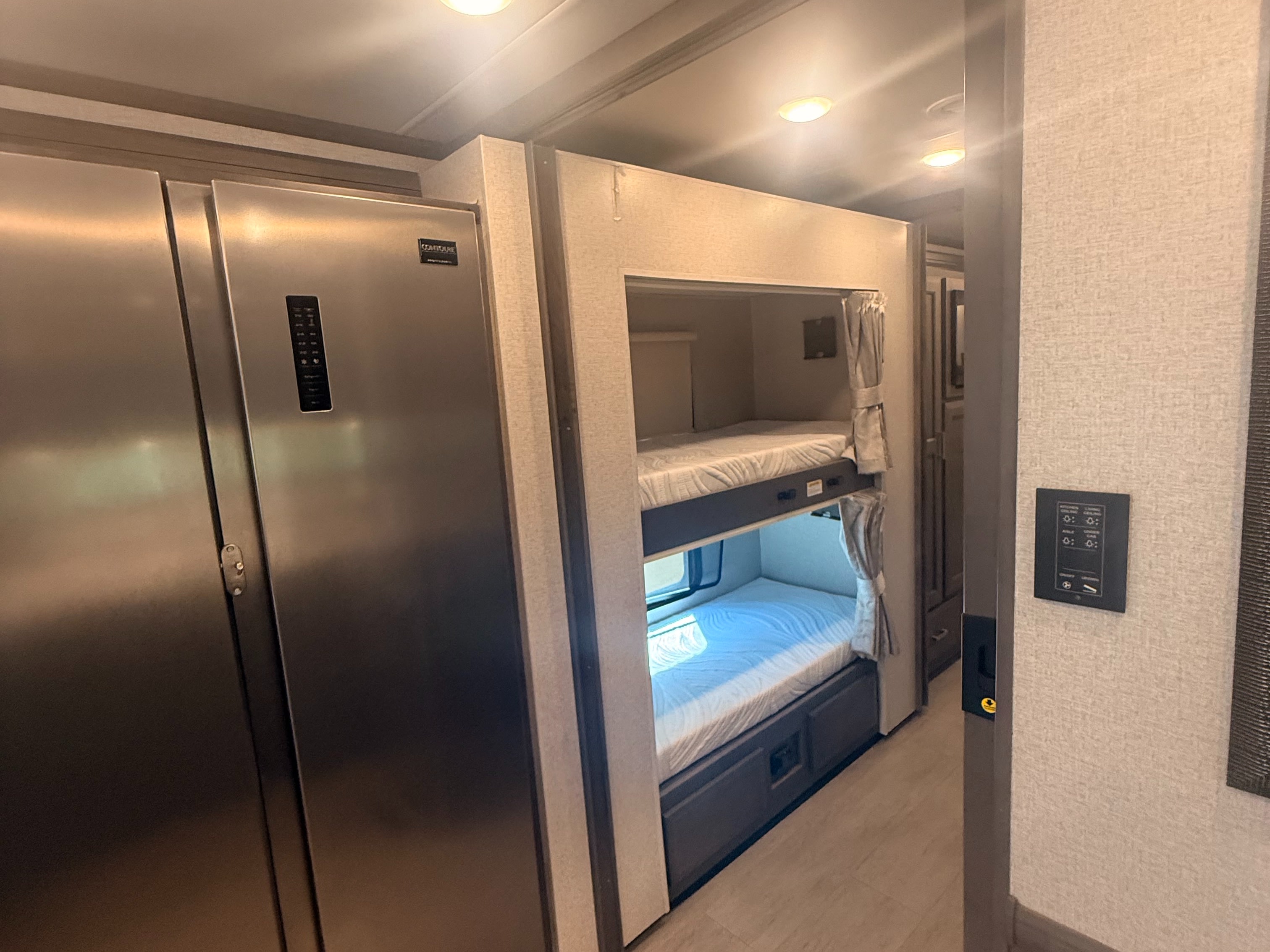 RV rental interior featuring a stainless steel refrigerator and cozy bunk beds with curtains, offering compact living space.. Thor Riviera 2024
