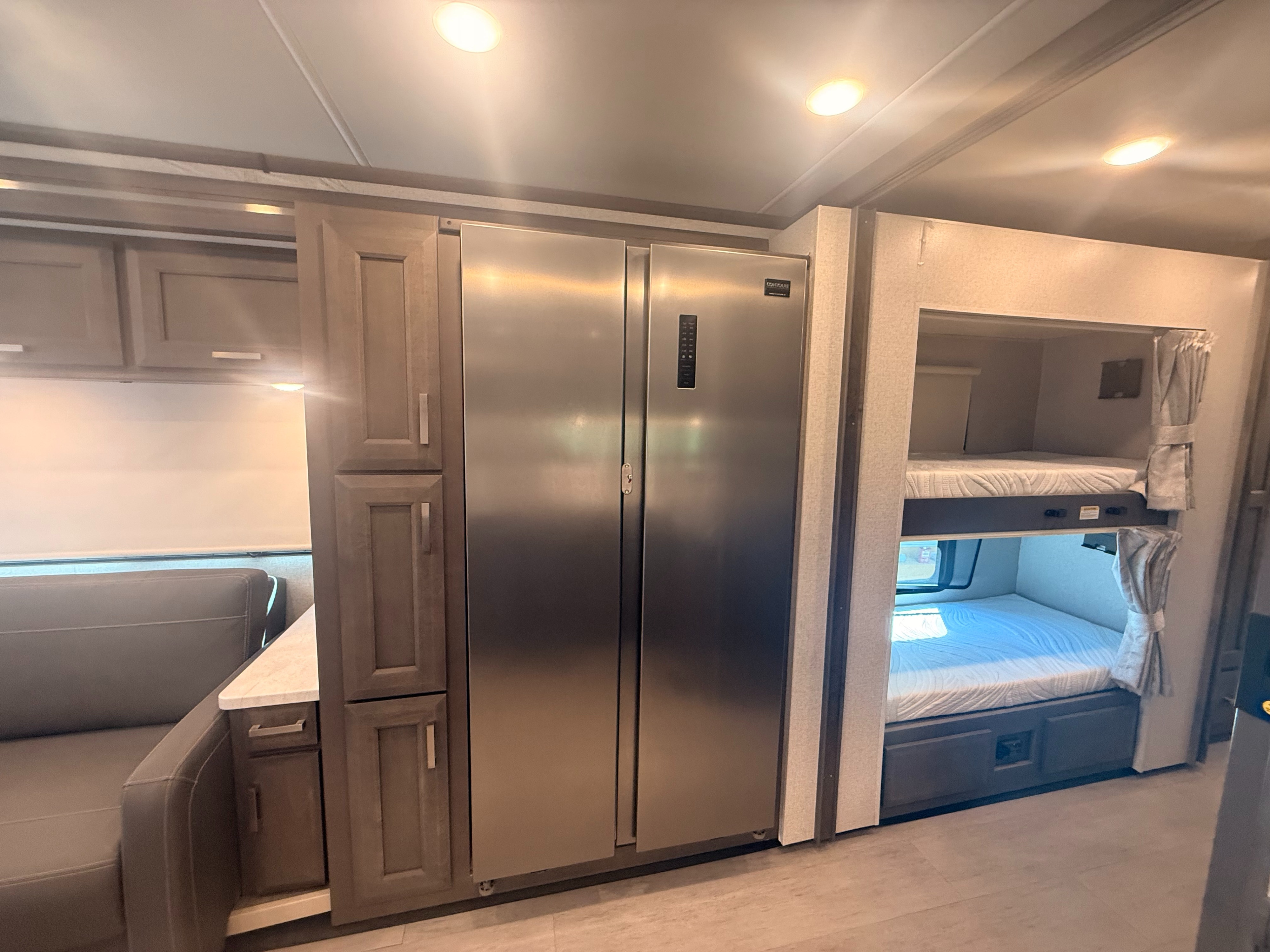 Spacious RV rental interior featuring a large stainless steel refrigerator, ample cabinetry, a comfortable sofa, and cozy bunk beds.. Thor Riviera 2024