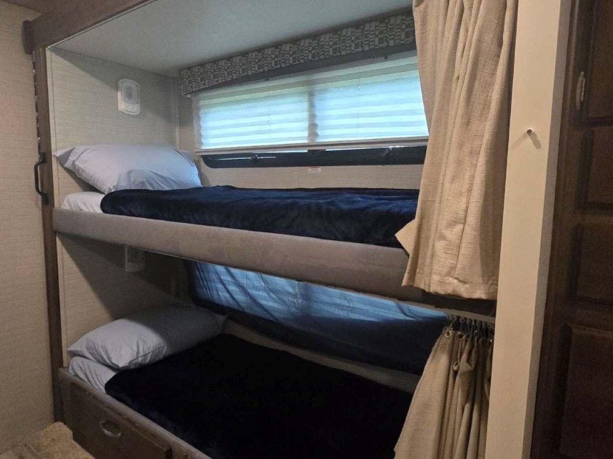 Cozy RV rental bunk beds, made with pillows & dark blankets, offer compact sleeping space for family travel inside.. Jayco Redhawk 2019